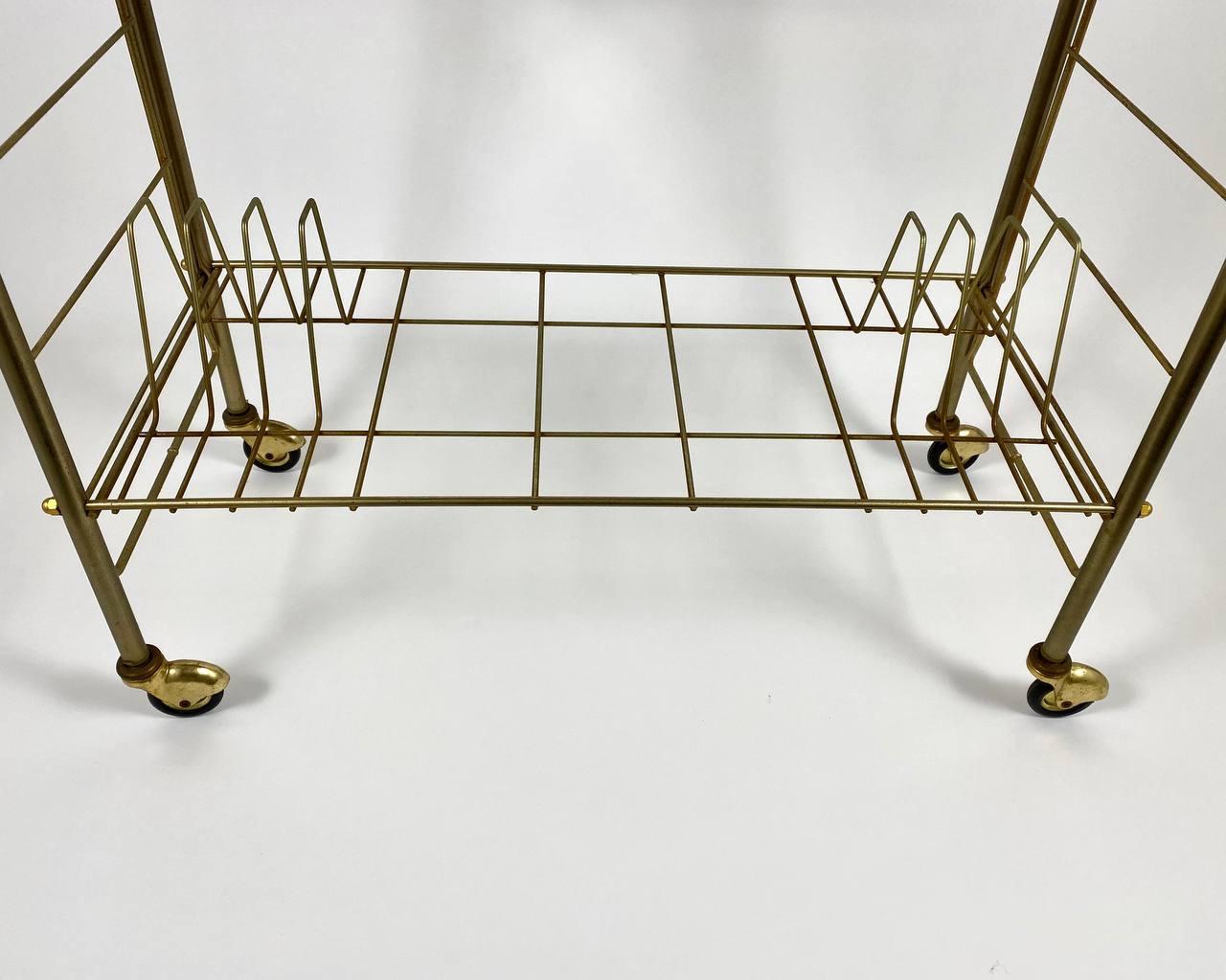 Vintage bar cart in formica wood and gold brass on wheels.

Germany. Stamped February, 1974.

Elegant serving table on wheels with a wood effect top and lower shelf for vinyl records storage, with a gold-tone metal base. 

Such a table is very