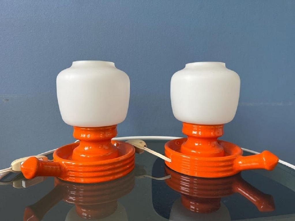 A set of ceramic pop-art table lamps with opaline glass shades. The glass shades are mat white and the base is orange ceramic. The lamps require one E14 lightbulb each and currently have EU-plugs (easily used outside EU with