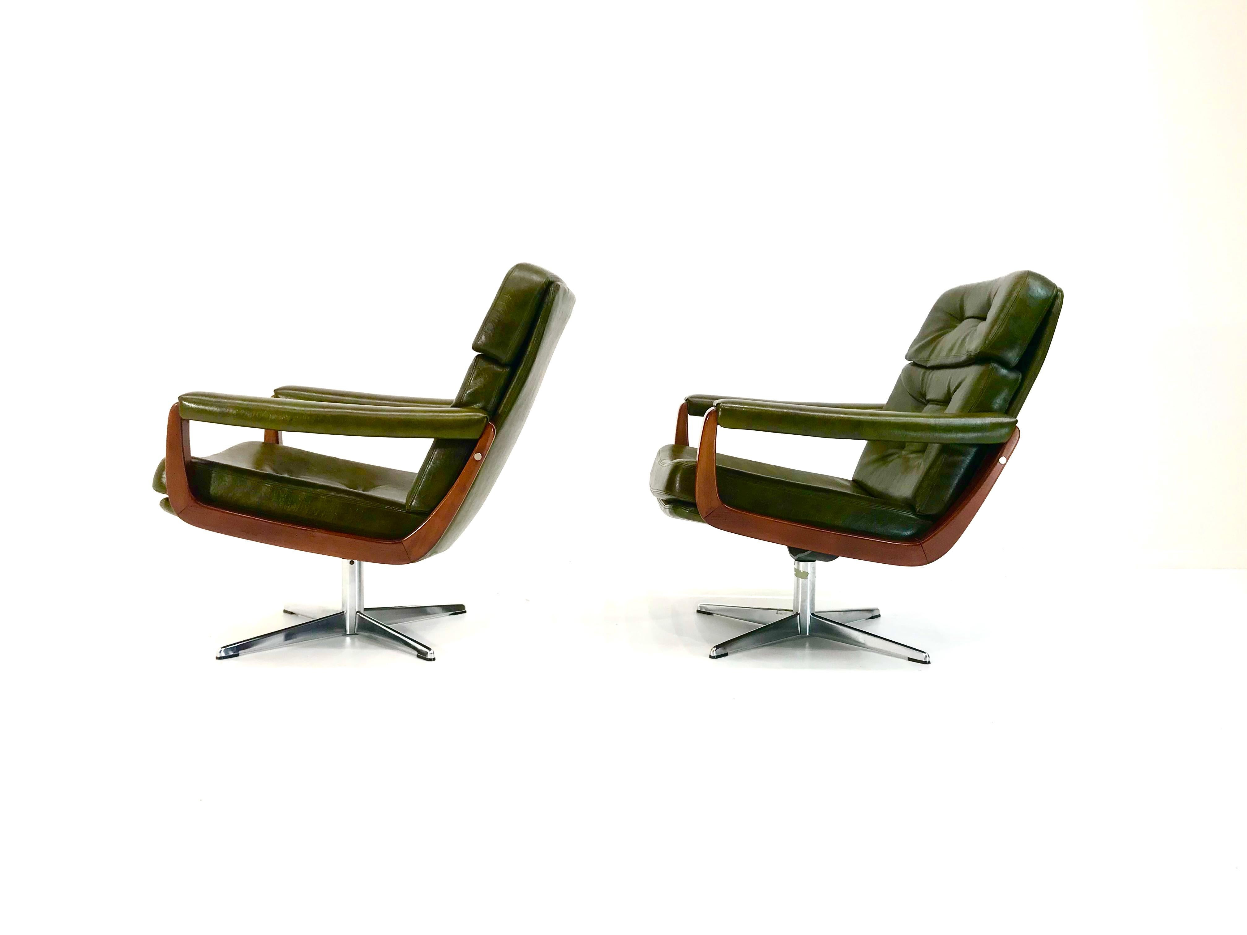 This is a vintage set of 2 senator lounge swivel chairs made in Denmark in the 1970s. The organic shaped armrests made of beech, the dark olive leatherette combined with the shiny cross legged base of cast iron create an outstanding 1970s look.