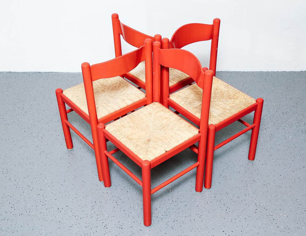 Bright red dining chairs with paper cord rush seats in the style of Vico Magistretti.
