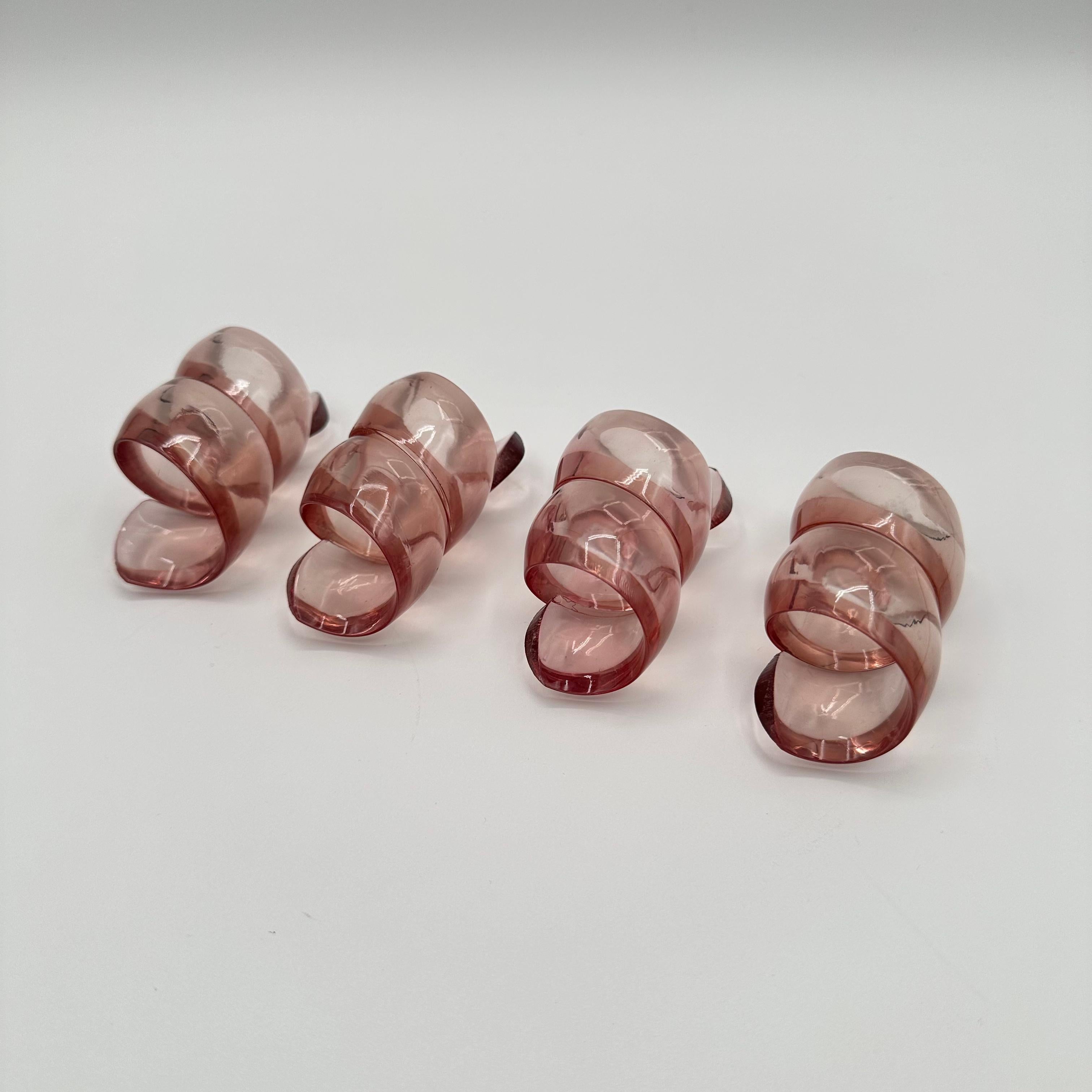 A vintage post modern set of four napkin rings in pink lucite, with a scrolling, looping, wrapping, ribbon or bow shape. Each of the 4 in the set is identical, providing a perfect feminine girly touch. 