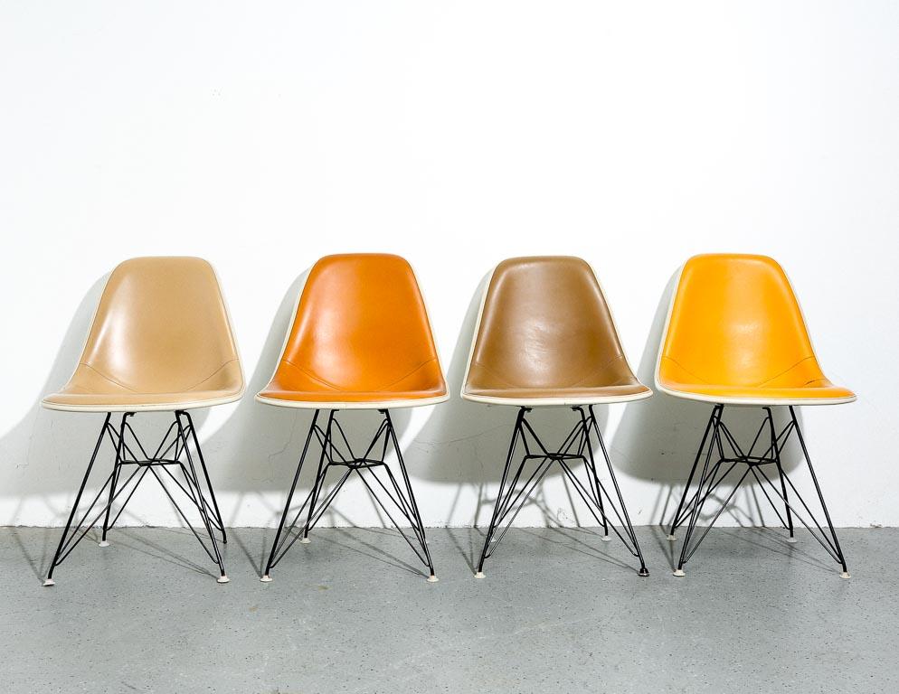 Vintage set of four Eames fiberglass dining chairs. Upholstered in orange, yellow, tan, and taupe Naugahyde. On original black eiffel bases.