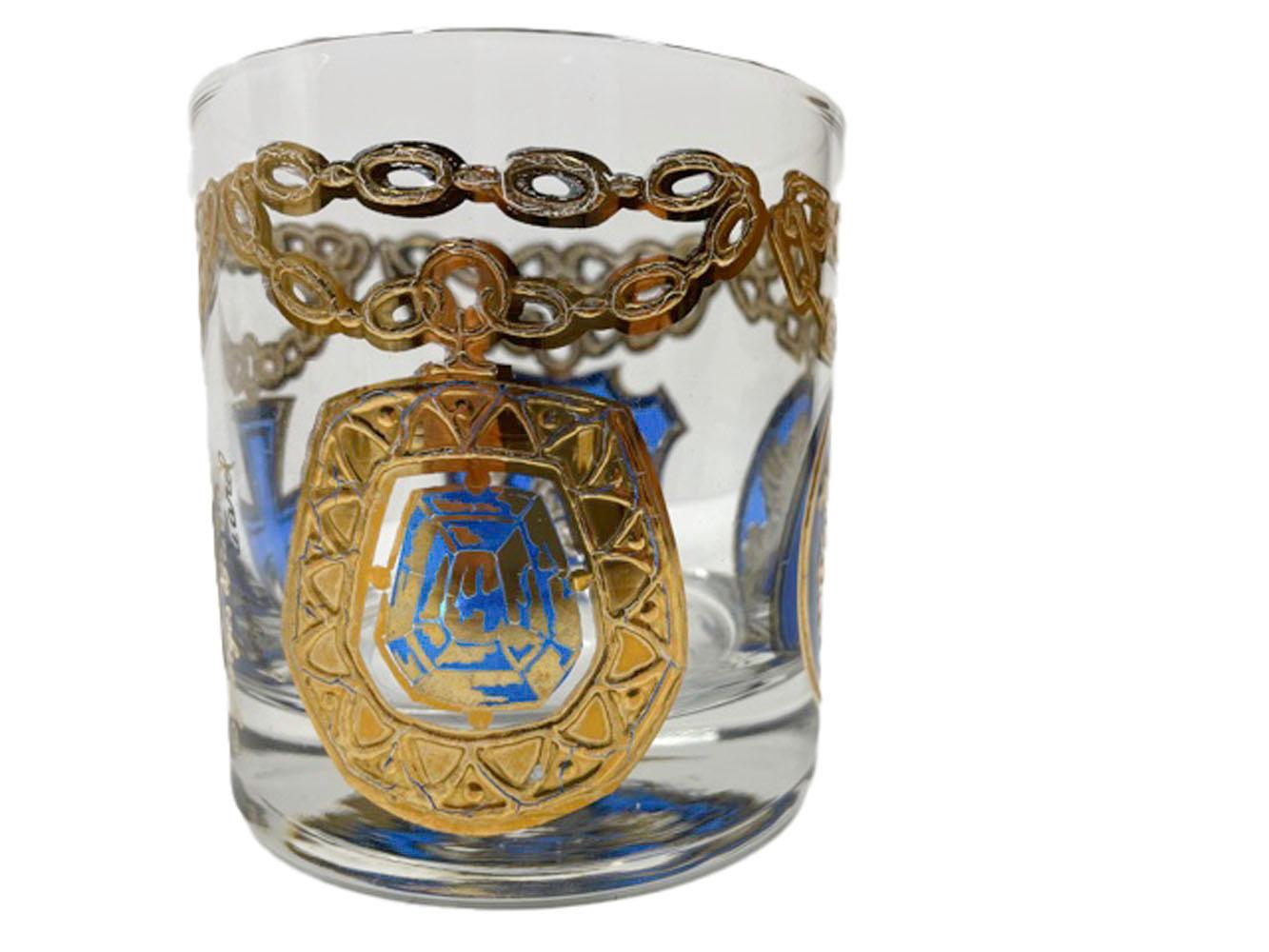 Four Georges Briard rocks glasses decorated in raised 22k gold and translucent colored enamels. Each of the four glasses with a different color enamel and having 4 different medallions hanging from chains around the exterior of the glass.