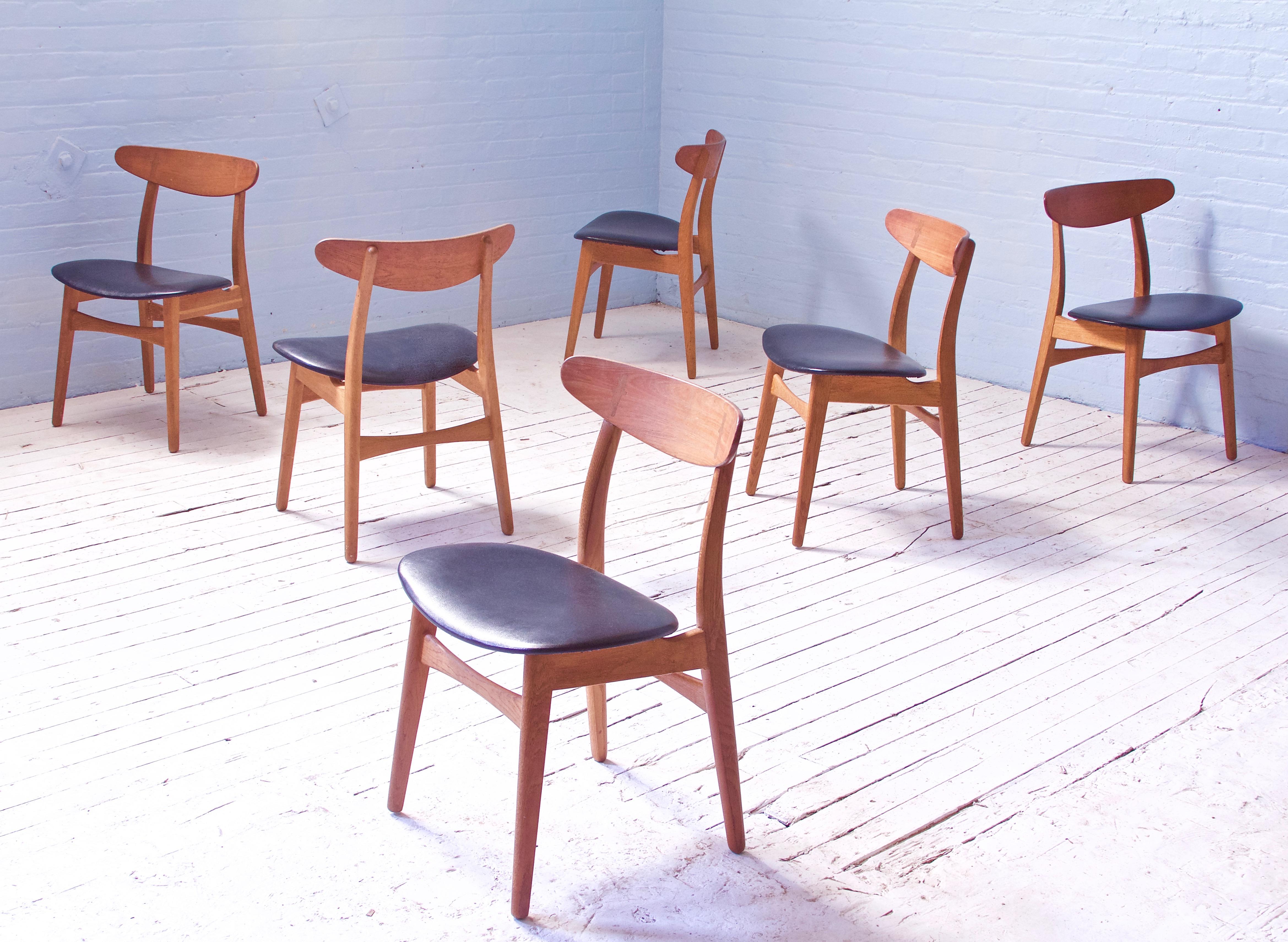 A lovely and well-preserved set of CH-30 dining chairs in oak and black vinyl. This model was designed in 1952 by a young Hans Wegner, and was one of the original five designs by Wegner created for and manufactured exclusively by Carl Hansen of