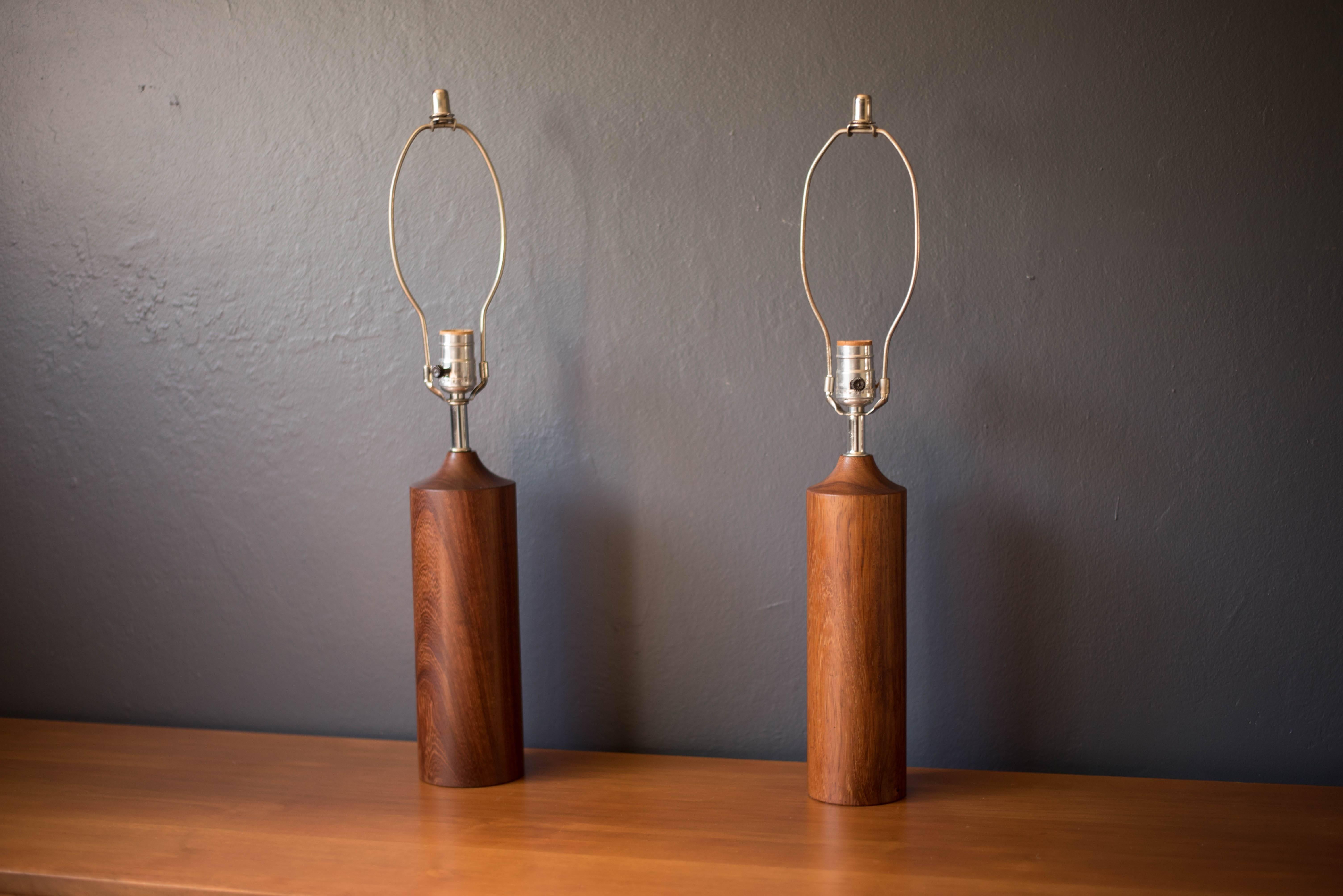 Mid century set of two table lamps in teak, circa 1960s. This set has a sculpted wood cylinder shape with chrome accents. The lamps slightly differ in size. Please see dimensions below. Price is for both lamps. 

Larger lamp: 3.82