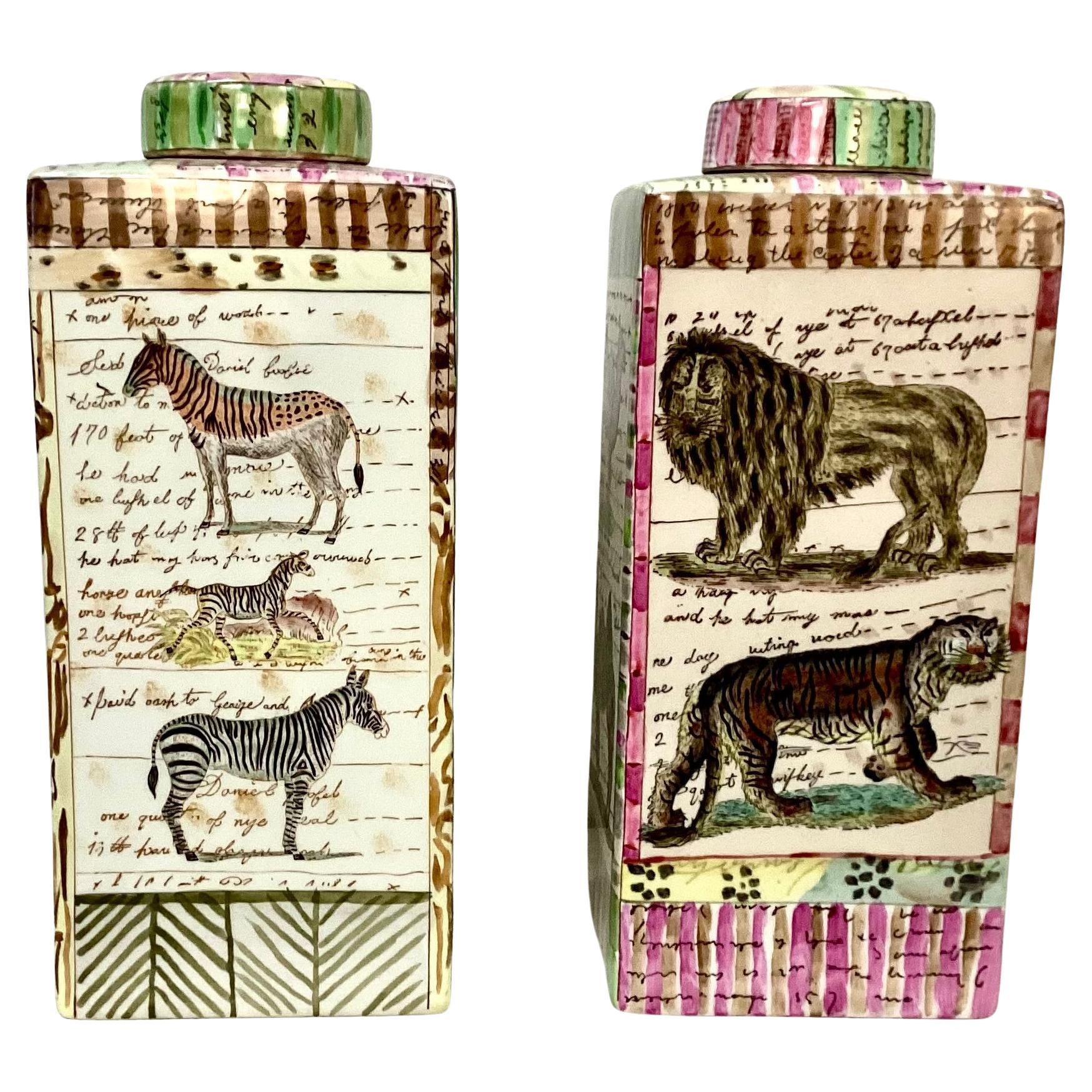 Pair of 20th century porcelain jungle-themed lidded jars by New York designer, John Derian. Elegant vases feature multiple jungle animals including elephants, tigers, monkeys and zebras set against script writing and stripes in pink, green and