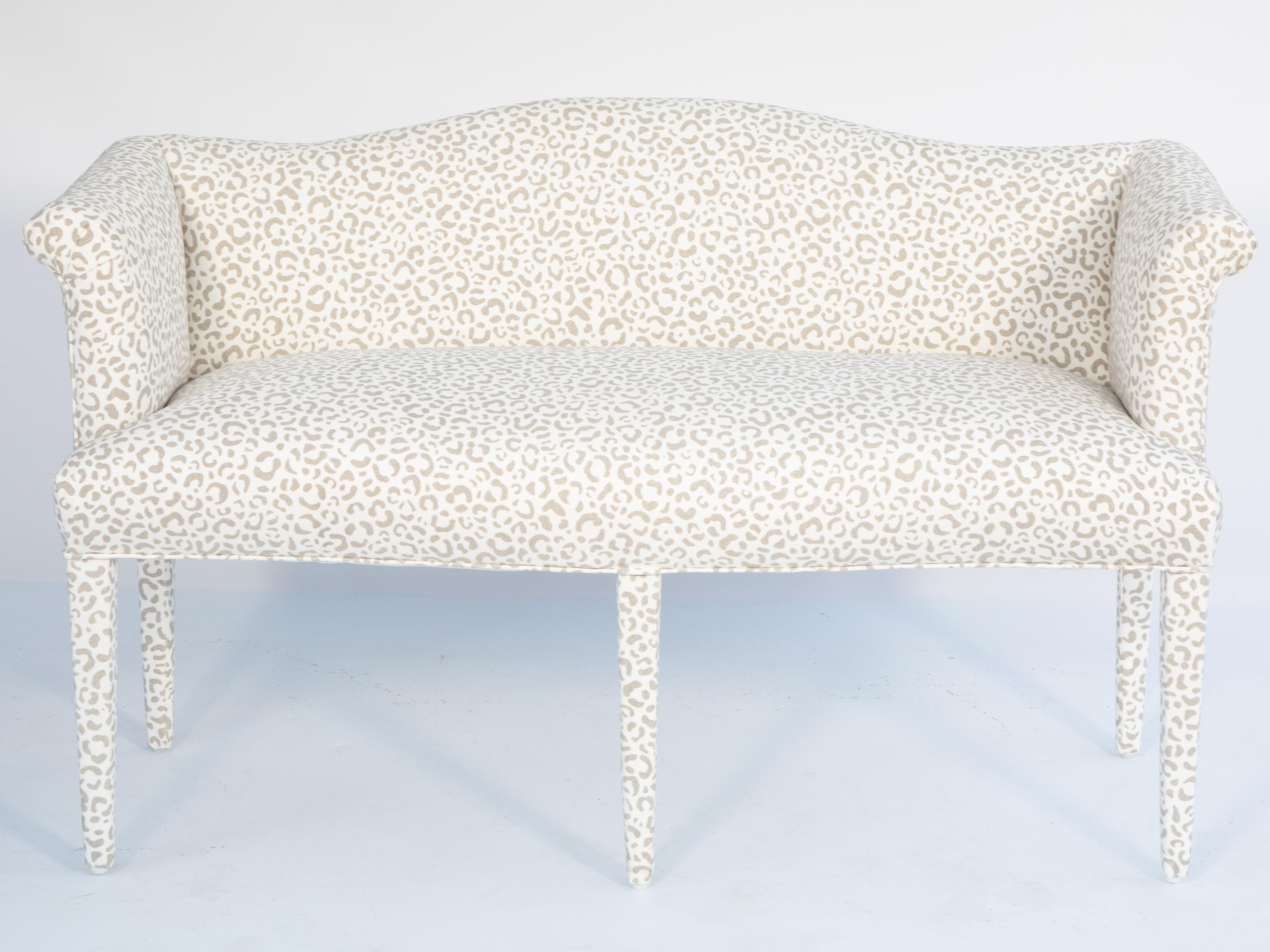 Vintage settee, completely upholstered in leopard-print denim fabric, having an arched padded backrest, and outscrolling arms, its crown seat raised on square tapering legs, with two matching throw pillows. 

Please contact us for alternative