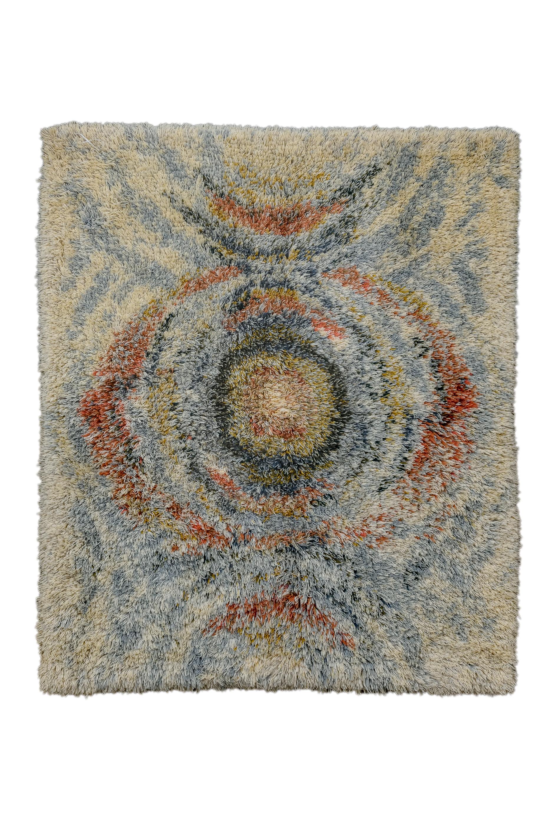 This exceptionally, shaggy long pile scatter shows a full and two upper and lower flanking halves, in a rough, concentric round manner, with swirls of red, straw, blue and beige. The central element seems to pulsate. A great rug for the coldest