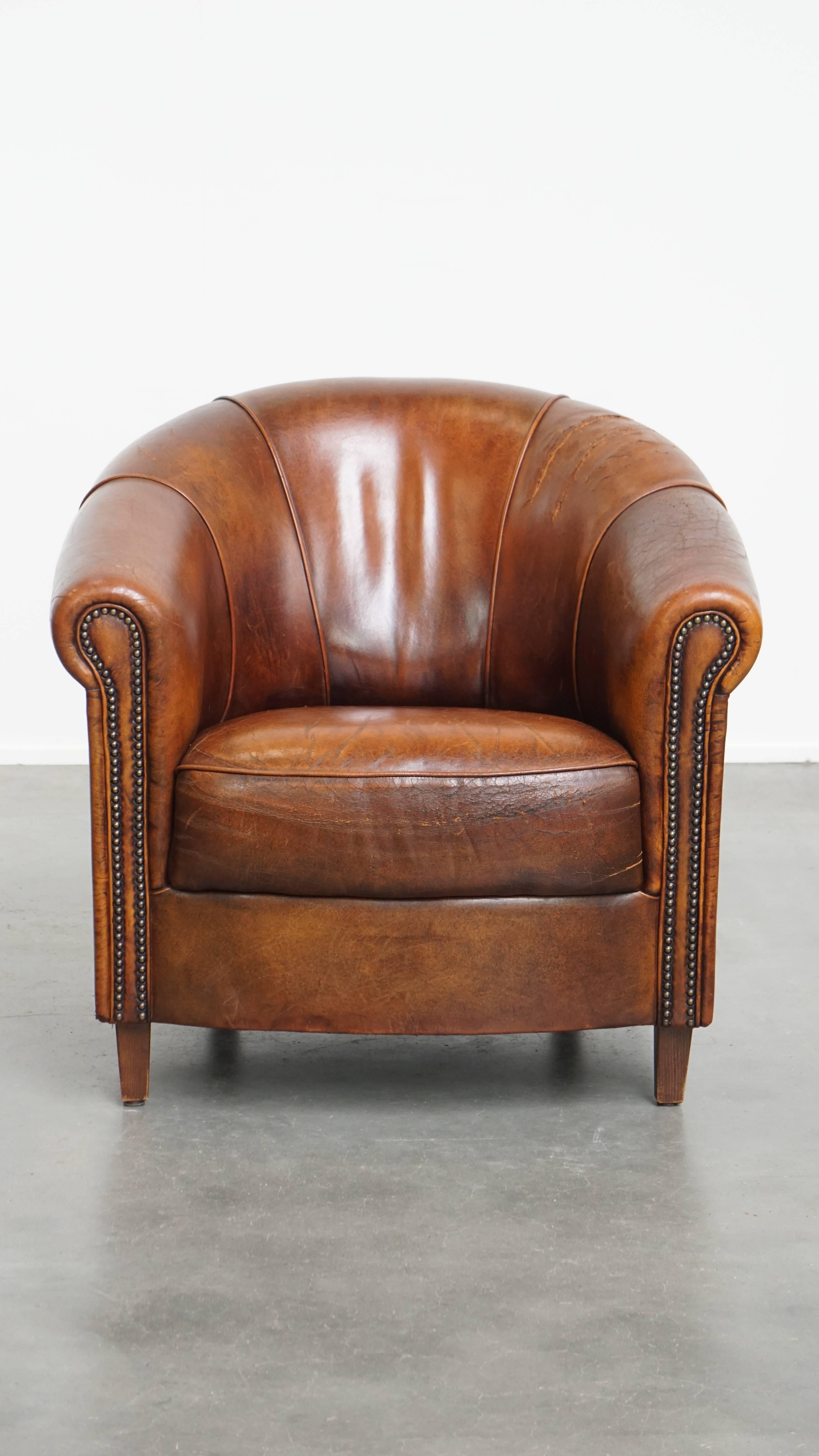 Offered here is this sturdy vintage sheepskin leather club armchair in beautiful warm colors, finished with decorative studs. This striking vintage armchair can be effortlessly placed in almost any interior. Over the years, it has acquired a