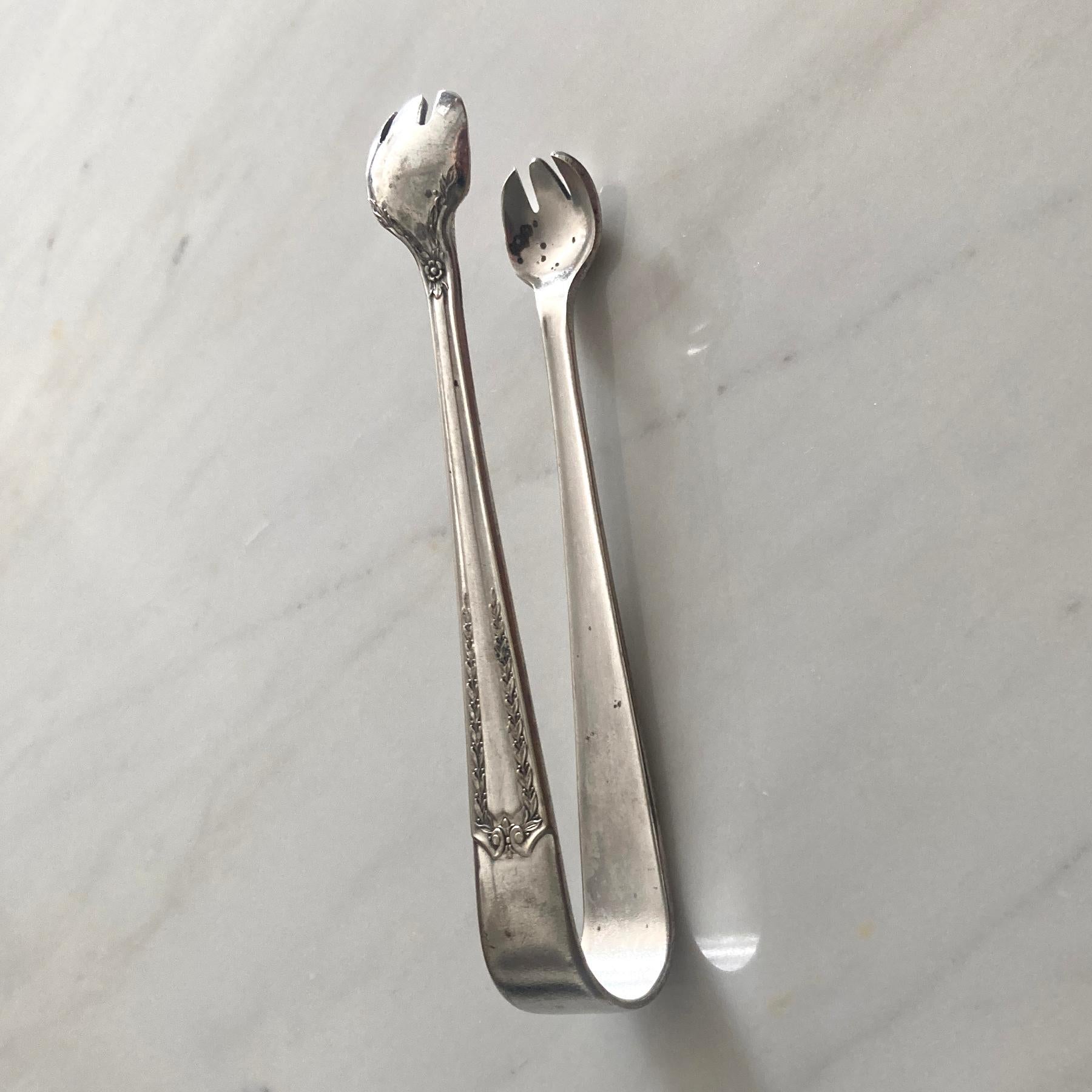 Esta encantadora pieza es de mediados de siglo. Las pinzas para azúcar de acero inoxidable son un acompañamiento elegante para tu próximo servicio de café o té. En ambos lados se aprecian elegantes y preciosas hojas florales y de rastro. 

En buen