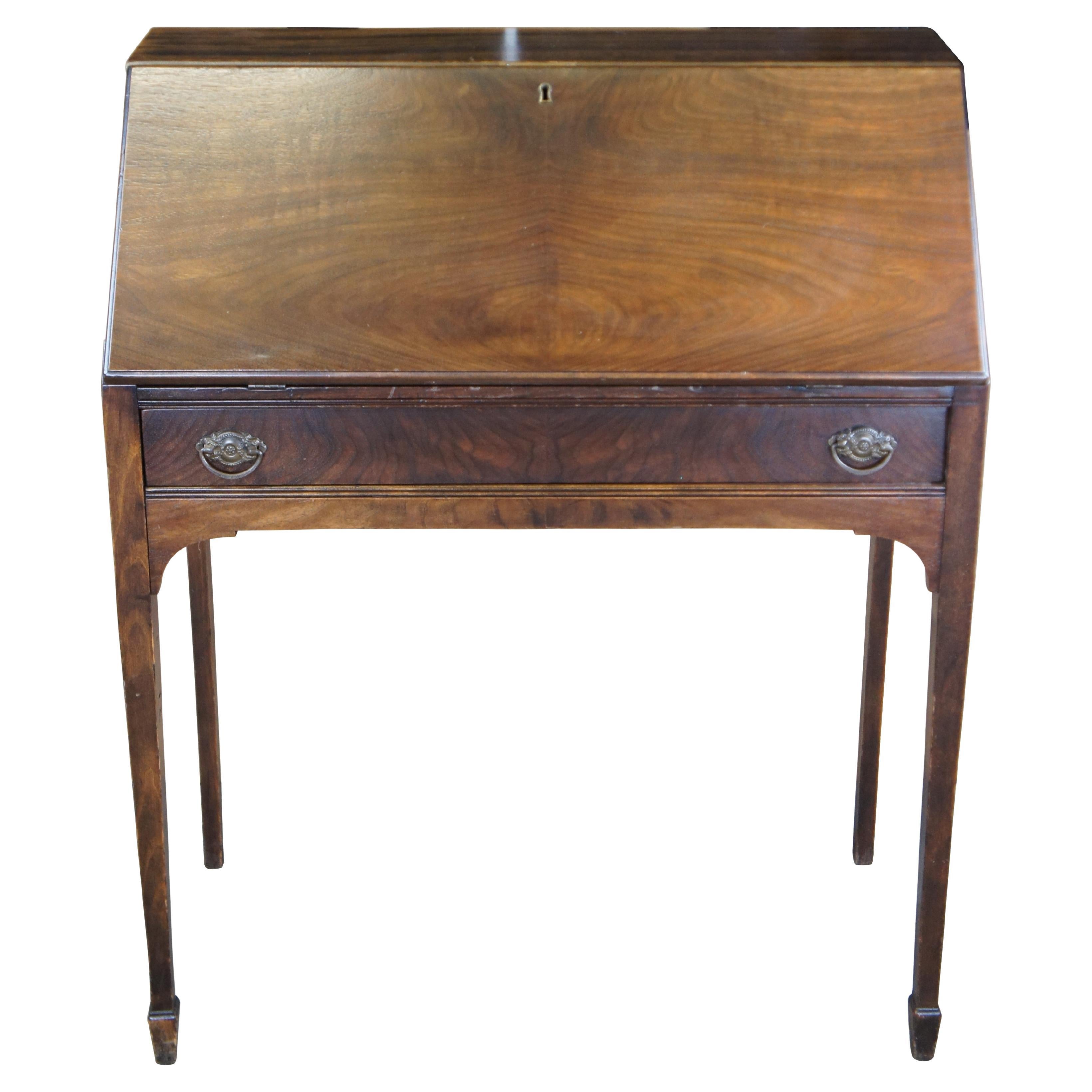 Sheraton style drop front secretary desk, circa 1930-40s.  Made from mahogany with a bookmatched lid opening to a writing surface with shelves and pigeon holes. Dovetailed storage drawer beneath writing surface has ornate brass hardware.  The desk