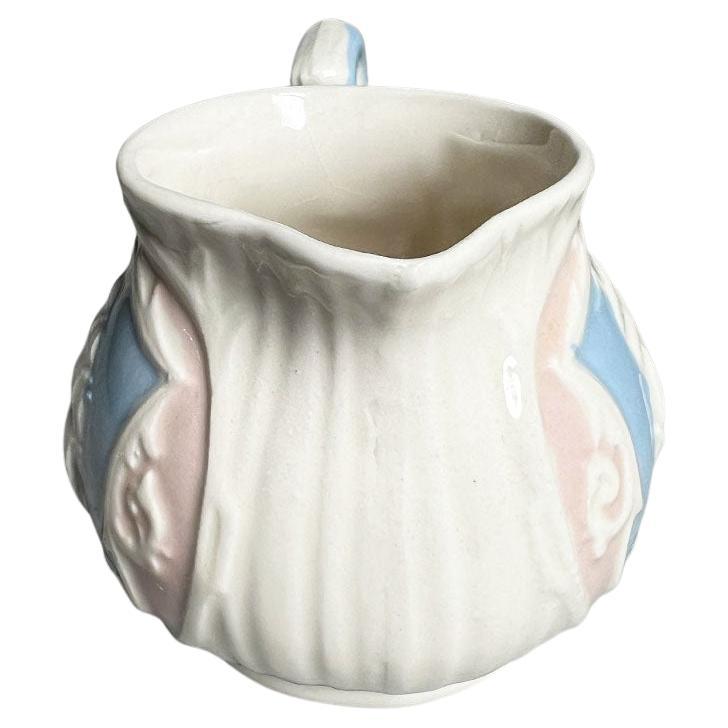 A small ceramic ship motif creamer pitcher. This piece features a ship with tall sails on a blue background with a pink border. The bottom is marked 