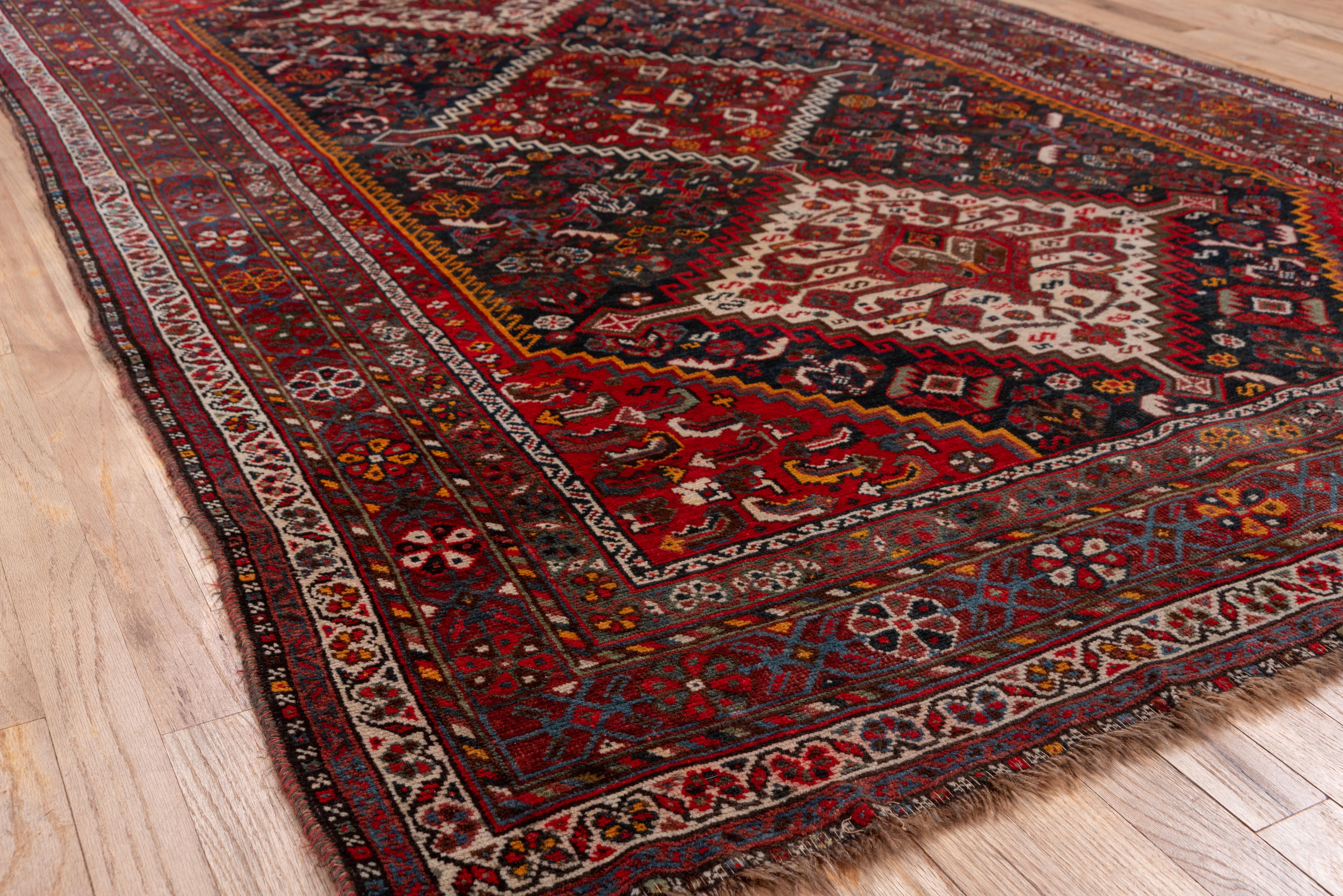 This vintage Shiraz rug boasts a bold tribal composition centered around a trio of diamond medallions set against a deep navy field. The design is enriched with symbolic motifs, including stylized birds, latch-hooks, and rosettes, all rendered in