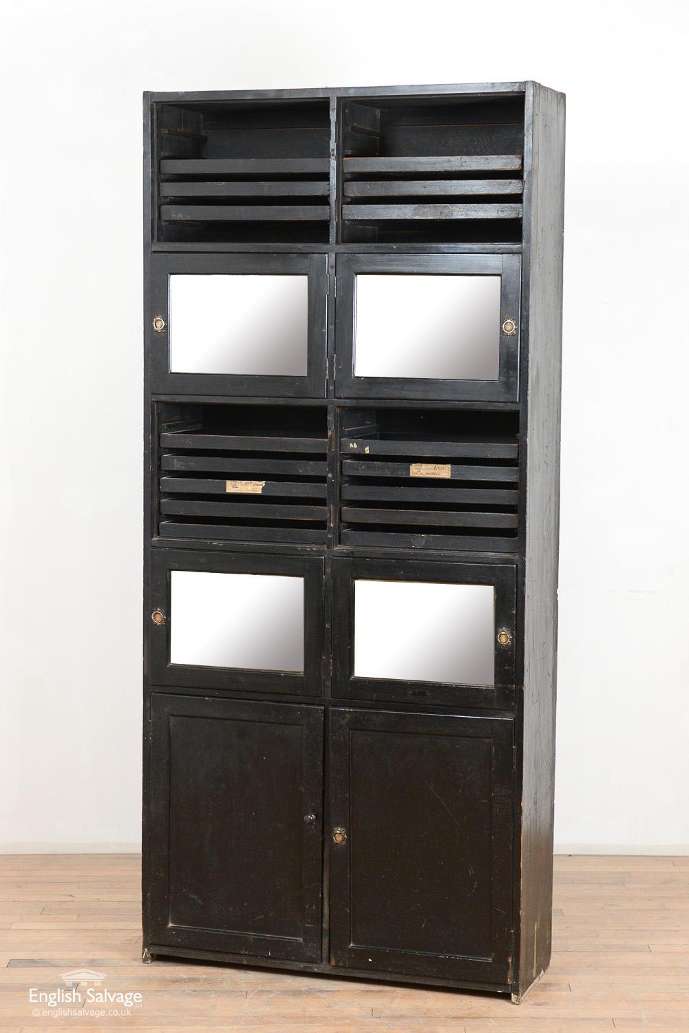 Unusual shop fitting display cupboard for jewelry or silverware. The black painted cabinet has two sets of mirrored doors, unusually hinged to open from the center of the cabinet rather than the edge. The lower cupboard doors are hinged at the edge