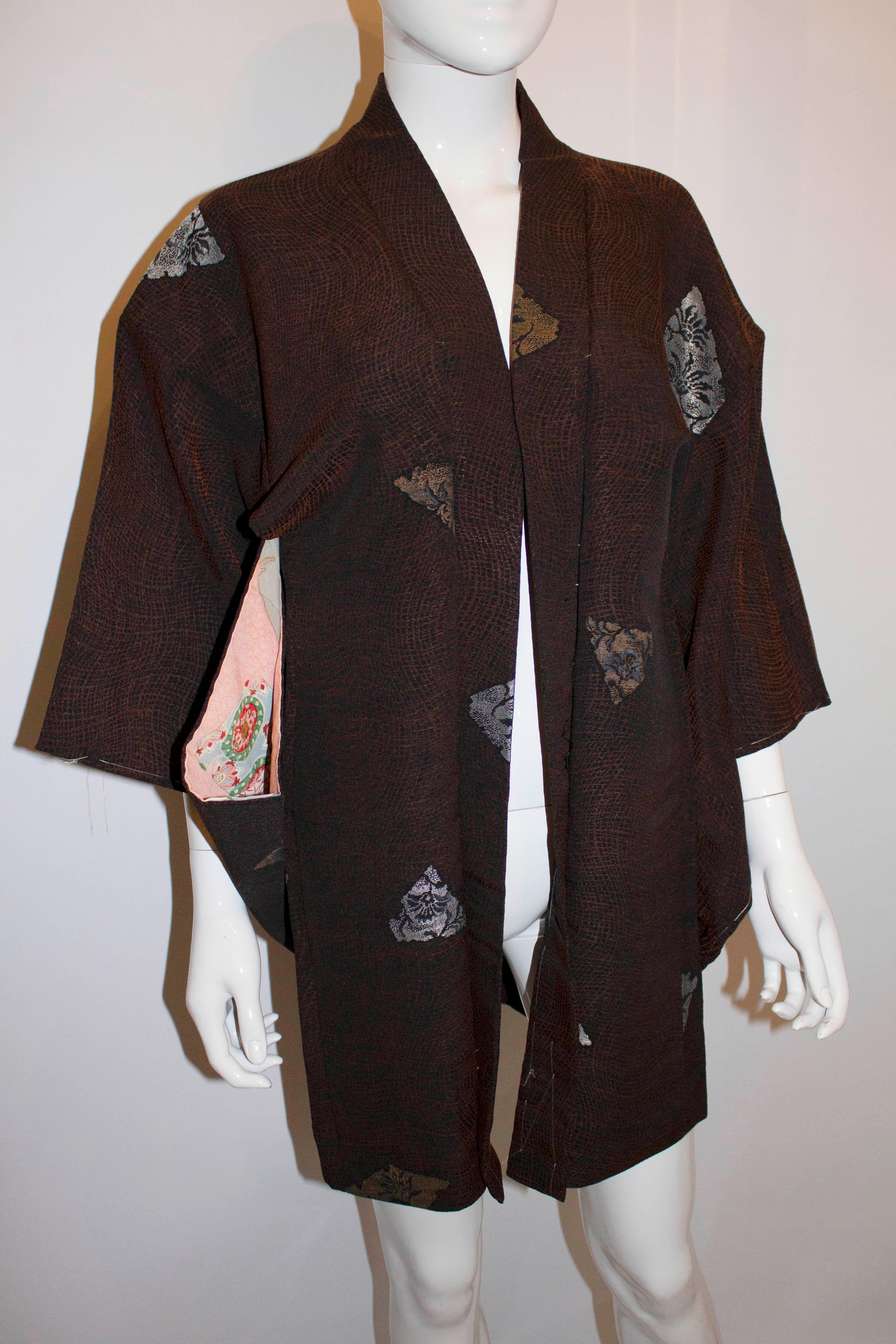 A short vintage kimono in black and brown woven brocade with a design of half open fans woven in gold 
 and silver. The kimono has a mons or family crest on the nape of the neck , and the kimono is lined in silk.
Measurements : length 33'' , bust up