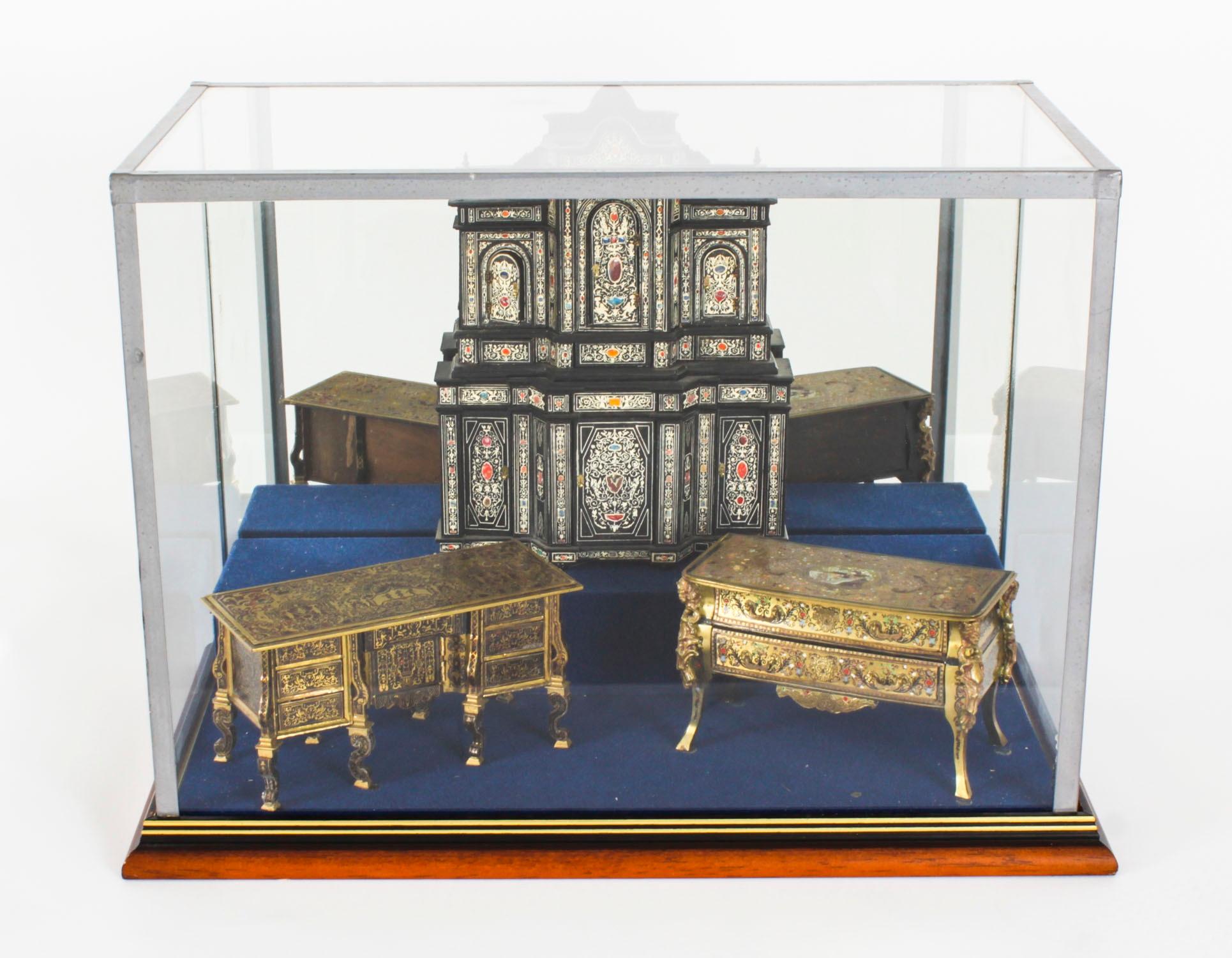This is a glass showcase containing fine vintage miniature models of French 18th century furniture, mid 20th Century in date.

It features a Boulle work style bureau mazarin, a two-drawer Boulle commode, and an ebonised cabinet with inlaid