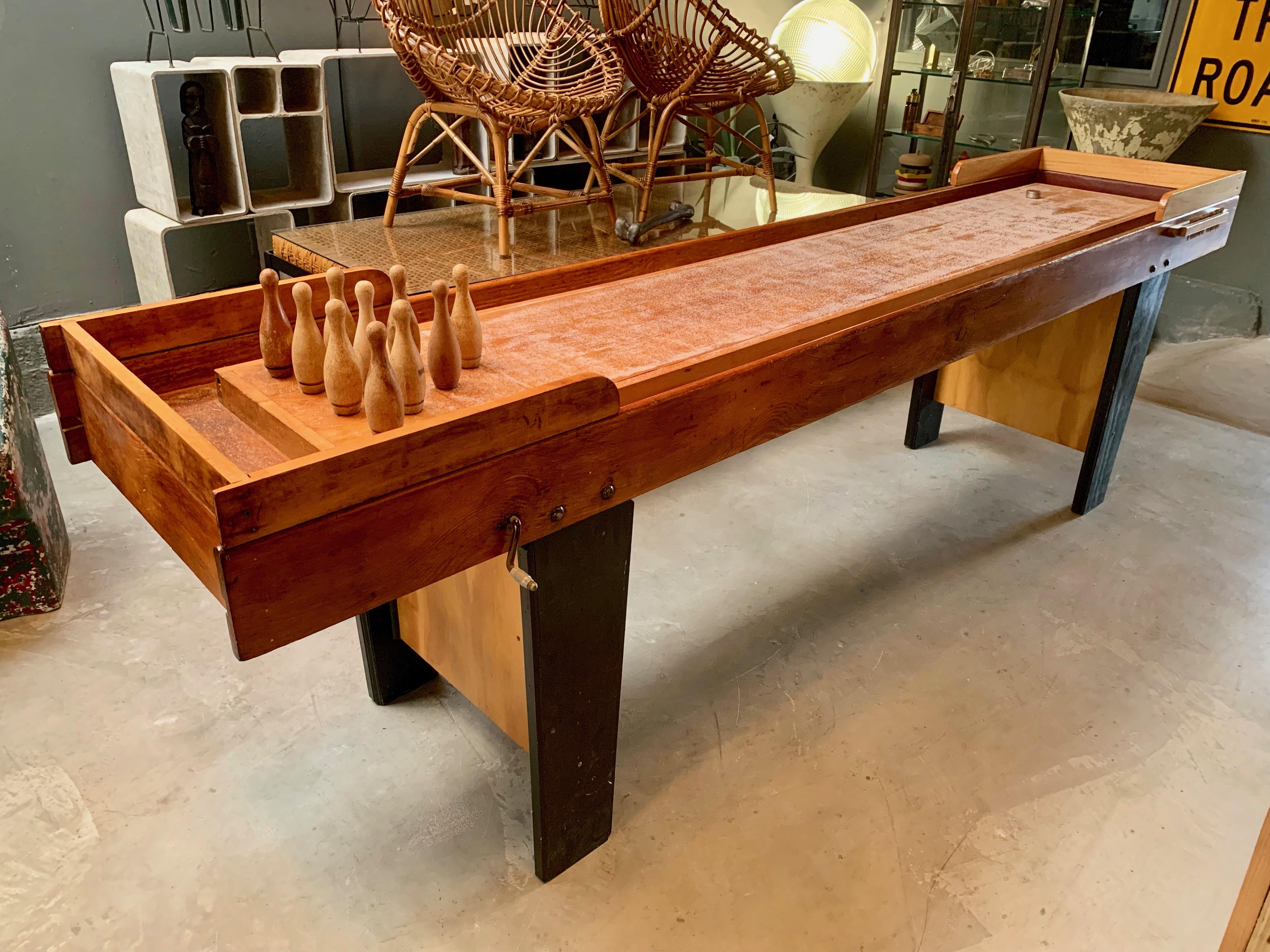 Cool vintage shuffleboard bowling table. Great lines and detail. Burgundy leather bumpers, wood pins and two-tone wood coloring. Interesting handle with manual mechanism that knocks over the remaining pins from underneath. Metal pucks included as