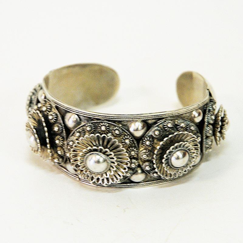 A lovely three dimensional silver cuff bracelet with decors of flowers, beads and balls design, from the 1940s Thailand. Half circle shaped and adjustable in and out.
American soldiers who visited Thailand in the mid-20th century bought this