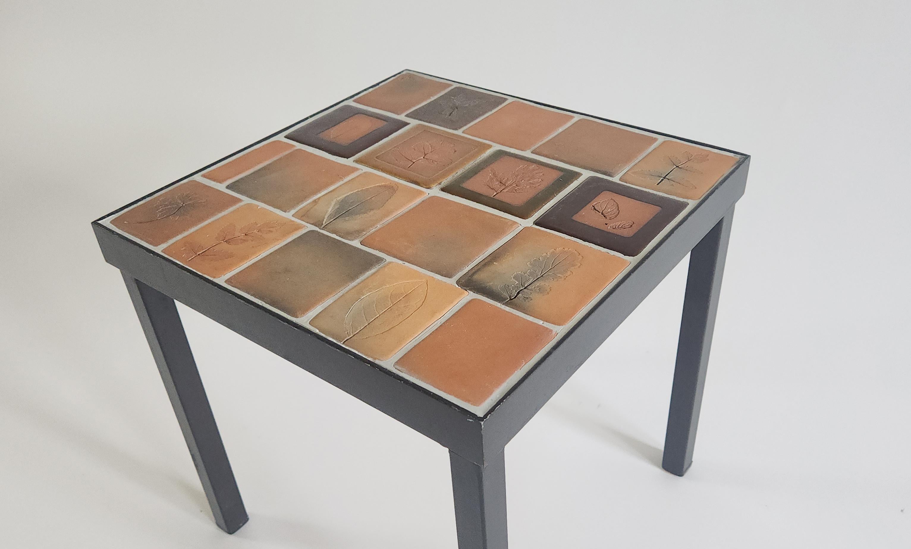 Side table with the famous Roger Capron Herbier tiles, designed from 1968 to 1982. The tiles are nicely underlined with a white grout. 

The handcrafted Herbier tiles were a subset of the Garrigue tiles produced by a technique in which real leaves