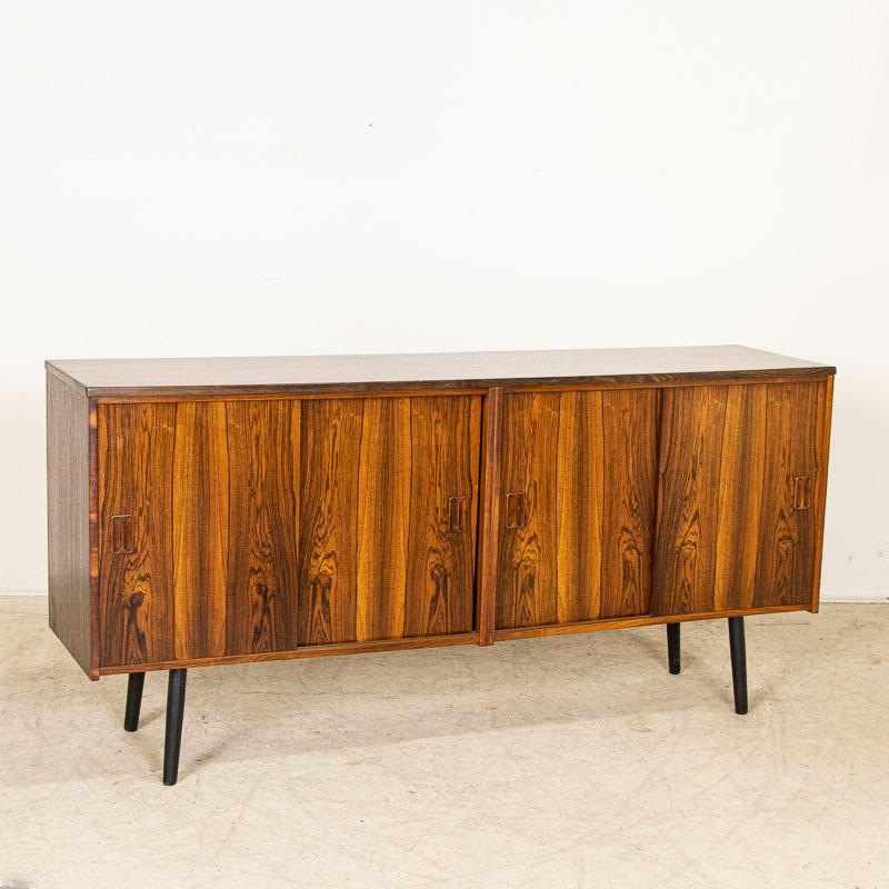 Low sideboard of veneered wood with four bypassing doors standing on slanted black tapered legs. This credenza has great presence due to the striking wood that was a style statement of the period and remains a fashion statement today. The two