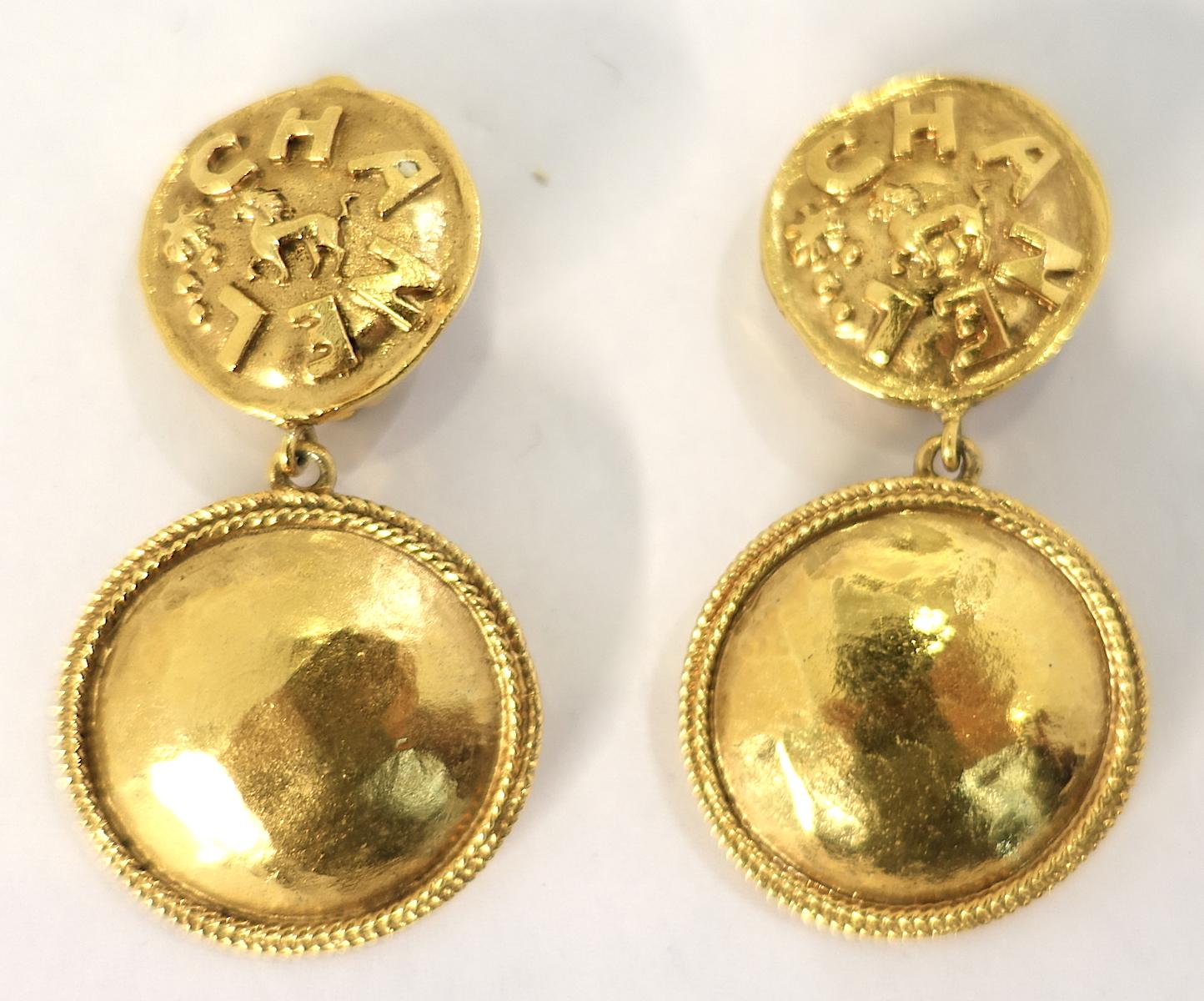 These vintage signed Chanel earrings have a circle top with “Chanel” written in a gold tone metal setting.  Hanging down is a larger circle with ribbing on the outside.  These clip earrings measure 2” x 1-1/8” and are signed “Chanel 23 Made in