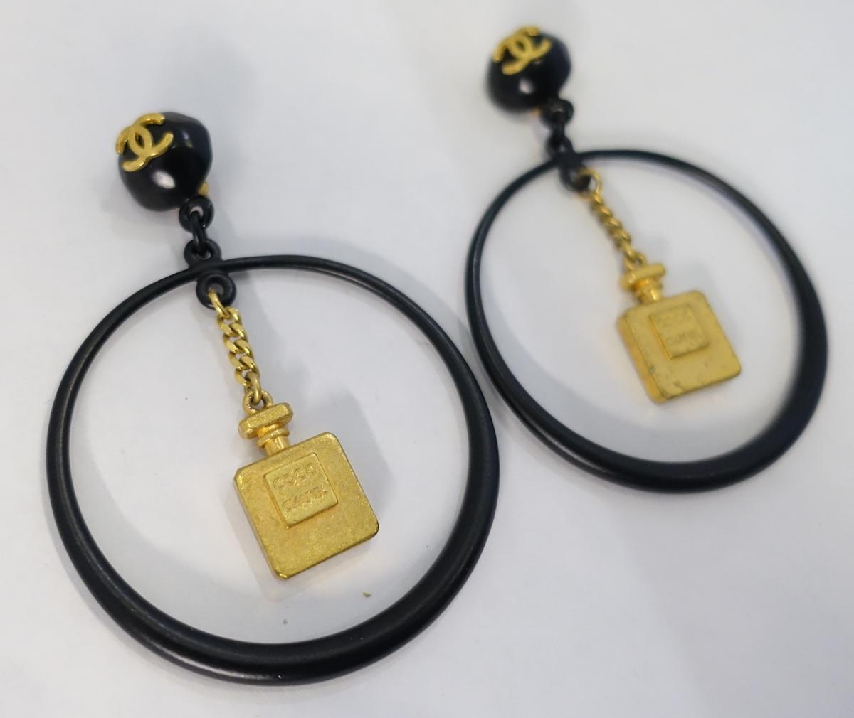 These vintage Chanel earrings are an in demand collectable.  They are designed with large black hoops with the famous dangling gold tone Chanel perfume bottle hanging in the middle.  The top has the famous double “Cs” on top. It is set in a gold