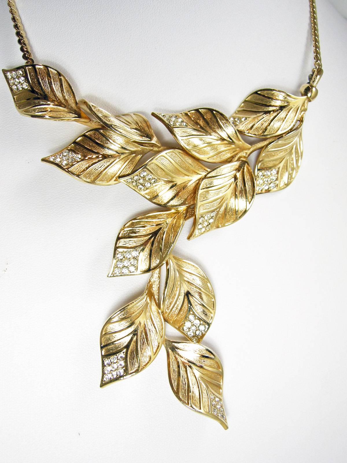 This Dior necklace has a sophisticated design with gold tone detailed leaves flowing downward.  At the end of each leaf are beautiful clear crystals.  It has a snake chain with a fold over clasp.  The necklace is 15” and the centerpiece is 4” wide