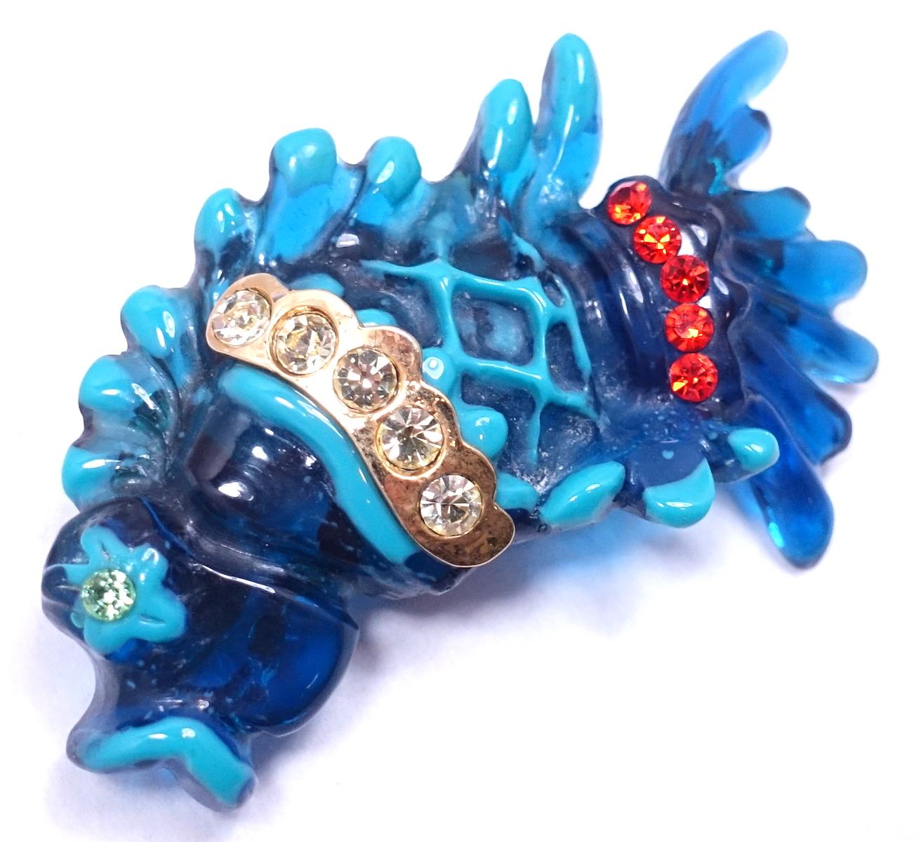 This impressive vintage signed Christian LaCroix jeweled fish brooch has different shades of blue with clear and red crystal accents …  in a gold tone setting.  This brooch measures 2-1/4” x 3-1/2”.  In excellent condition, it is signed “Christian