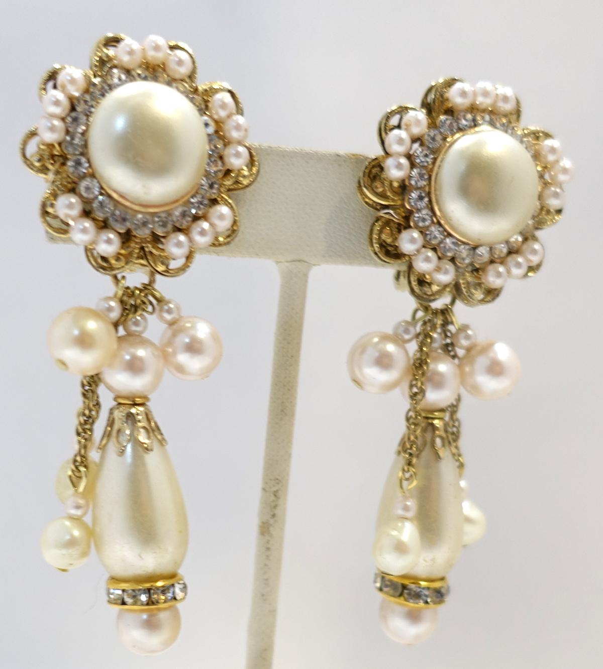 These vintage signed DeMario earrings has a faux pearl top with crystal accents. A large faux pearl hangs down with a gold tone cap and faux pearls above. In excellent condition, these clip earrings measure 3” x 1” and are signed “DeMario”.