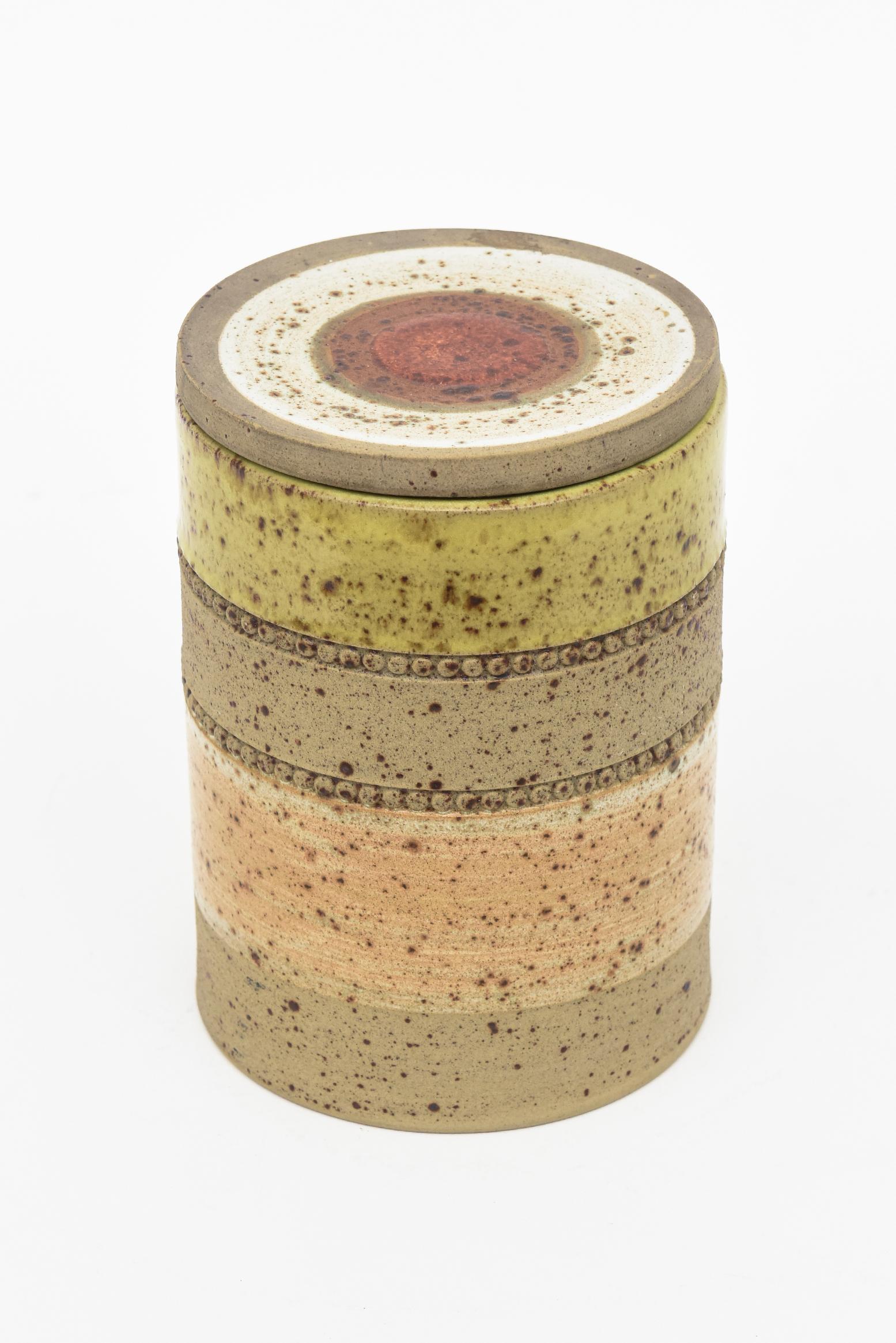 Diese schöne runde Keramikdose mit Deckel ist mit Denby Made in England gekennzeichnet. Es ist eine Kombination aus glasierten und unglasierten Farben von breiten Streifen mit 2 Perlenreihen. Das Oberteil hat ein rotes Bullauge in der Mitte, das mit