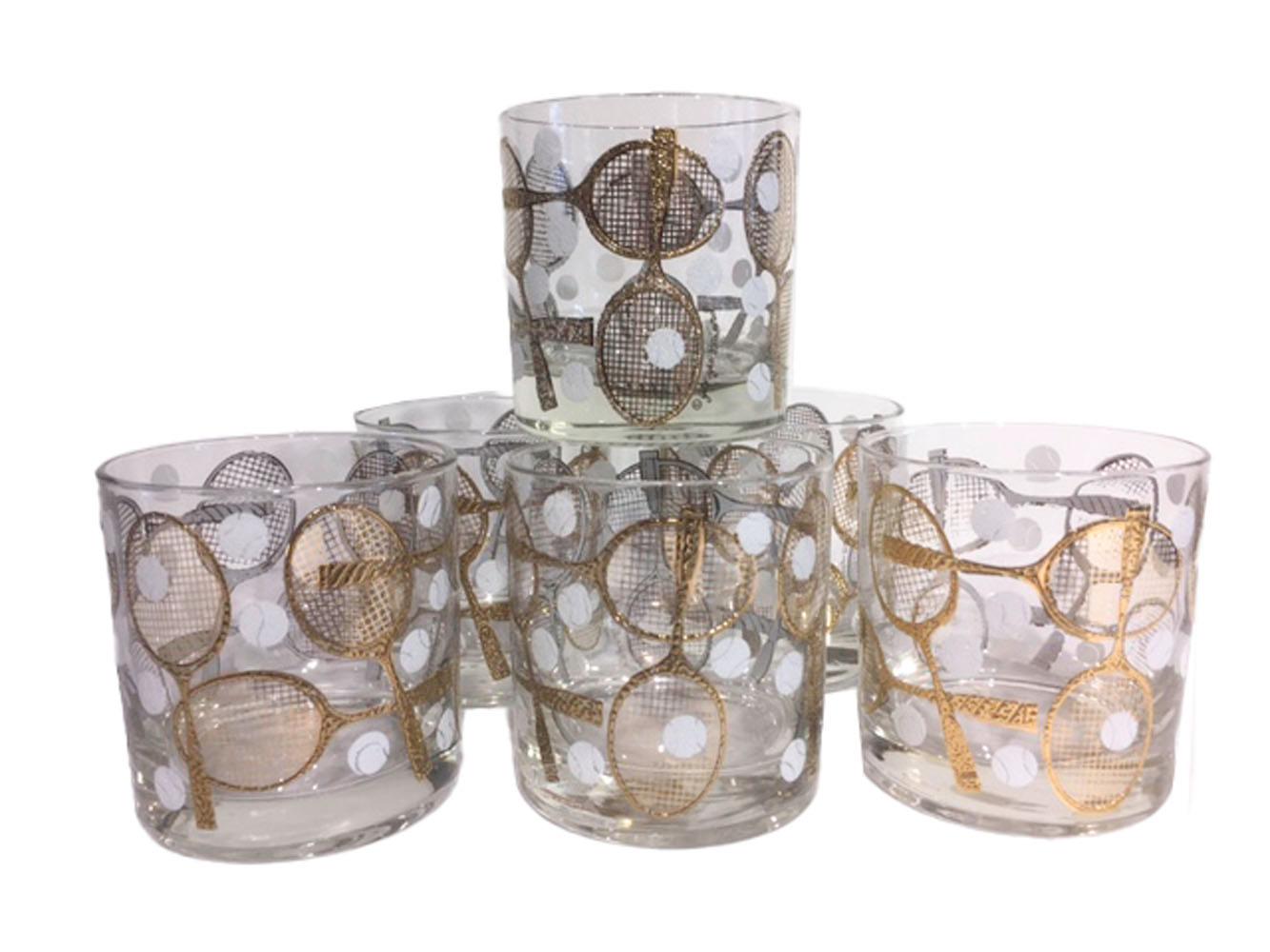 Mid-20th century rocks glasses designed and signed by Georges Briard, decorated with tennis racquets and balls in 22-karat gold and white enamel. Together with a companion cheese board or serving tray in walnut with an inset white enamel tile with