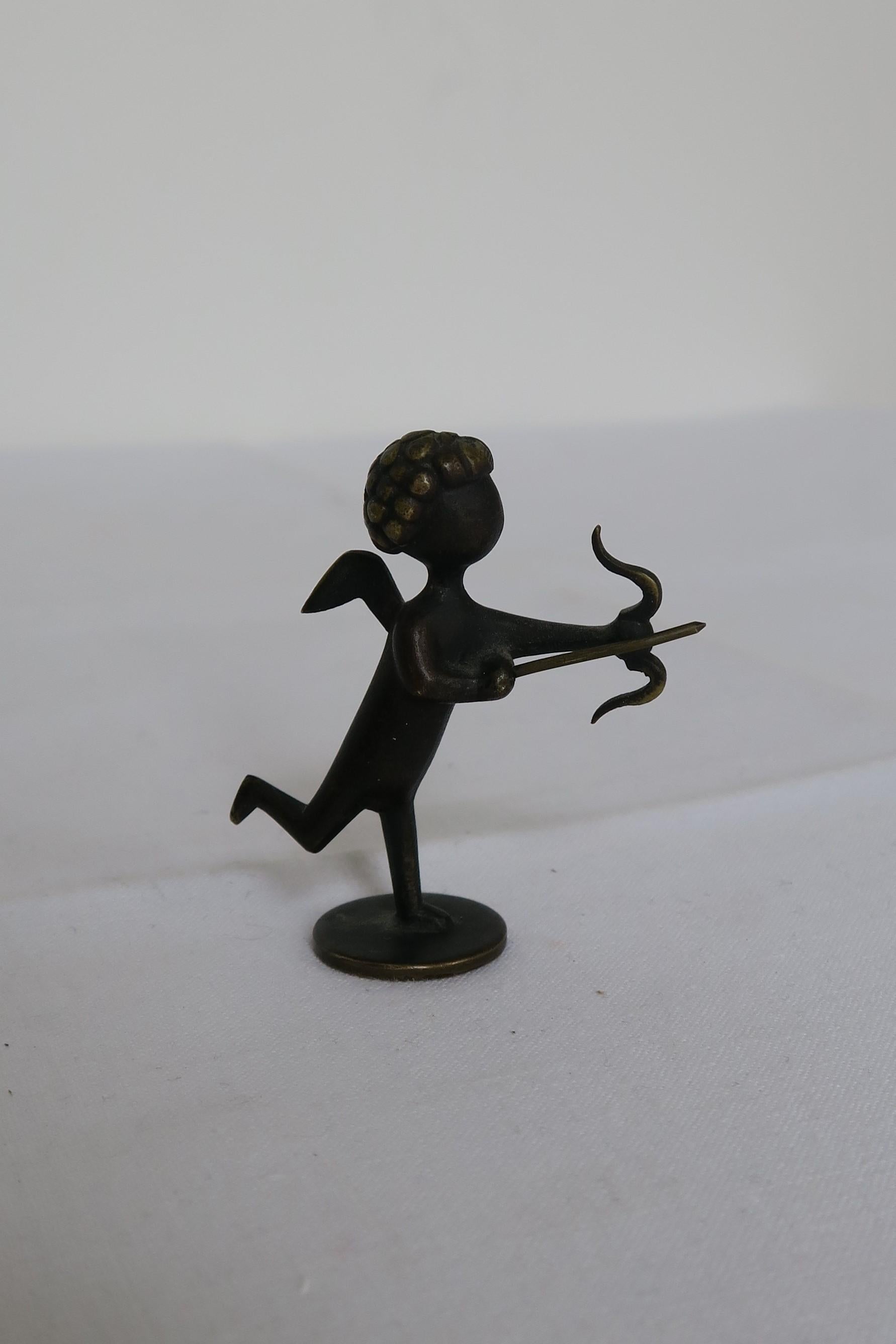 The item on sale is an original vintage bronze figurine. It was designed and manufactured by the Austrian workshops of Hagenauer. The Figurine represents a little cupid with bow and arrow in Mid-Century Modern style. It is stamped and in presteen