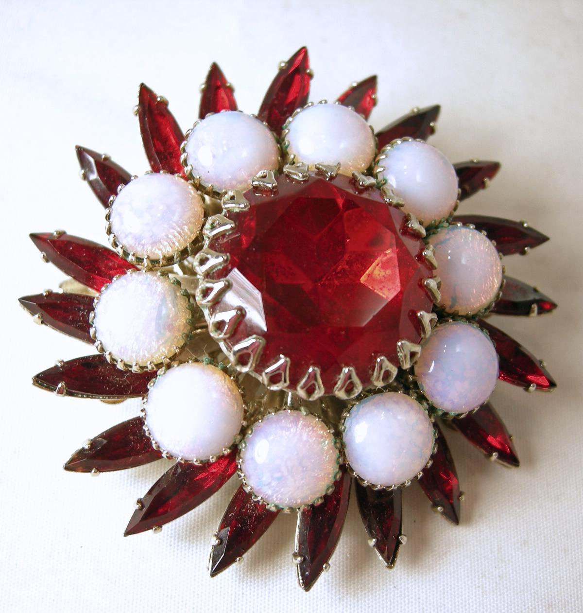 This vintage signed Judy Lee brooch and earring set has a pinwheel design with a bright red crystal center and faux opals surrounding it and ended with red crystal marquis.  The brooch measures 2” and the matching clip earrings are 1-1/2”… all in a
