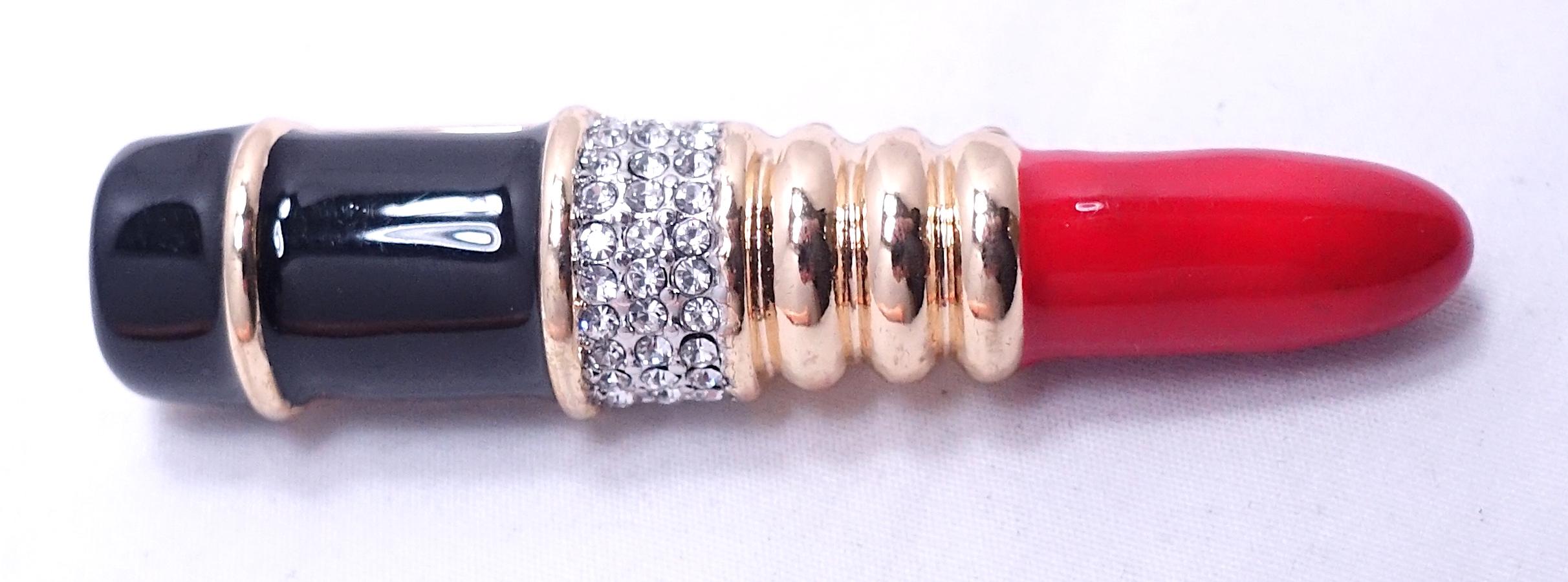 This famous vintage bookpiece lipstick brooch was made by Kenneth Jay Lane.  It features red and black resin with clear crystals in a gold tone setting.  In excellent condition, this brooch measures 2-1/2” x 1/2” and is signed “KJL”.
