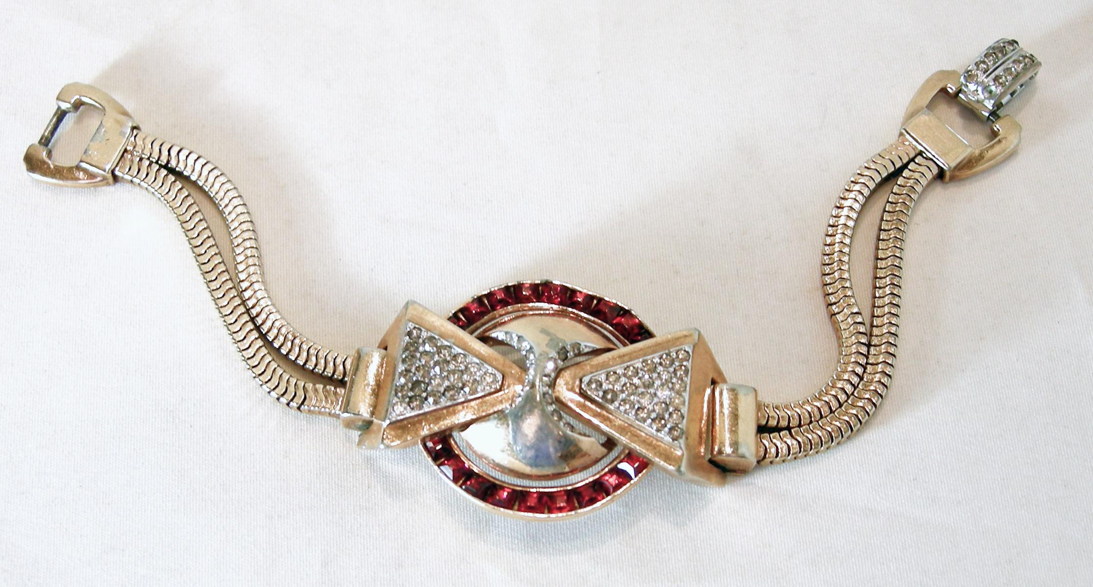 This vintage bracelet by Mazer screams Art Deco.  The center has faux rubies that are channel set in the middle circle design. On each side there is a crystal encrusted triangle pointing inward to a gold tone ball center.  The double chain leads to