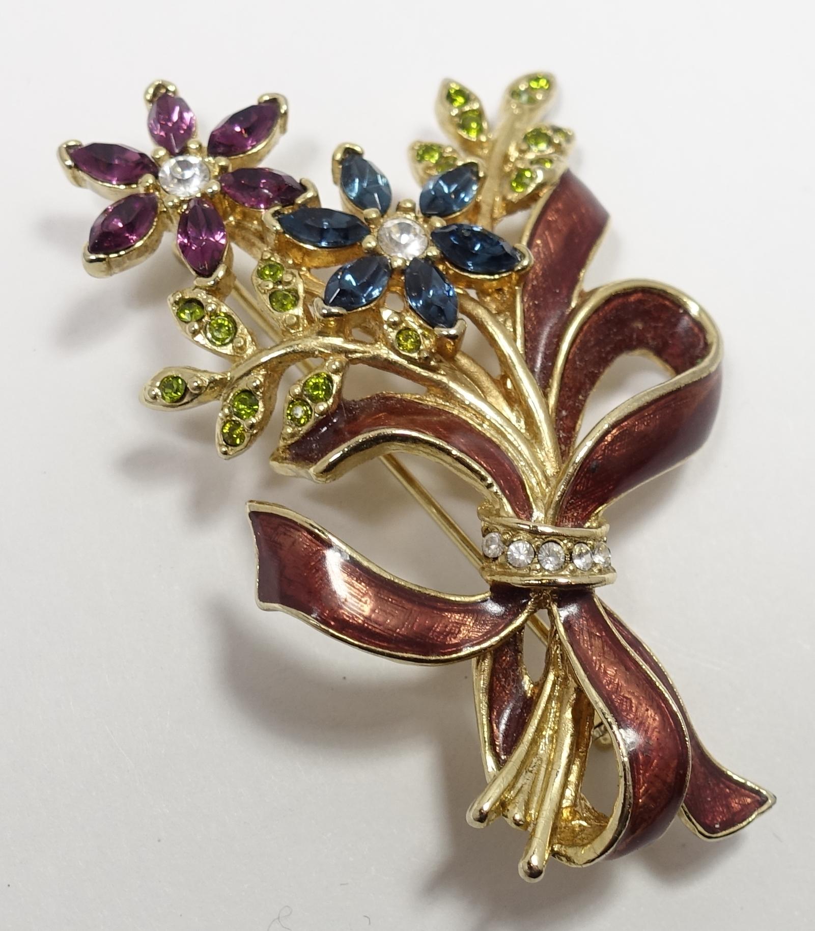 This vintage signed Monet brooch has a floral design with blue, peridot, purple and clear crystals with enameled ribbons circling the gold tone stems.  This brooch measures 2-5/8” x 1-3/4” and is signed “Monet”.  It is in excellent condition.