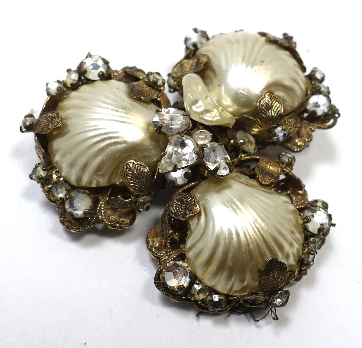 This vintage signed Original by Robert brooch from the 1950s has 3 faux pearl seashells with small faux pearls and clear rhinestones on the outside and center. It is in a gold tone setting.  In excellent condition, this brooch measures 2” x 2”, and