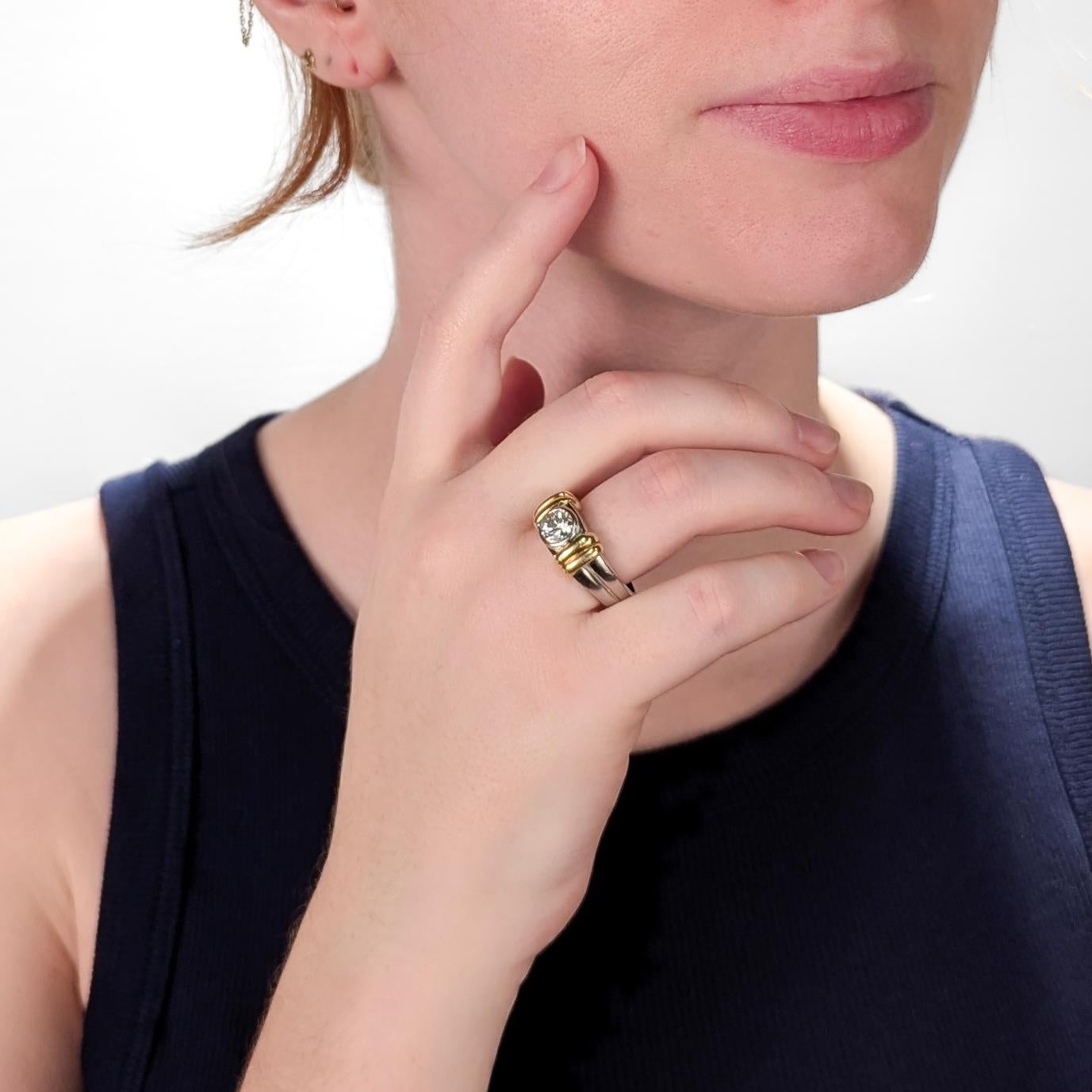 A fine signed platinum, gold, & diamond ring.

In .950 platinum with 18 karat yellow gold elements.

With a central bezel-set 1.20± Ct diamond flanked on either side by bulky gold accents to the shoulders.

Marked to the shank.

Accompanied by a