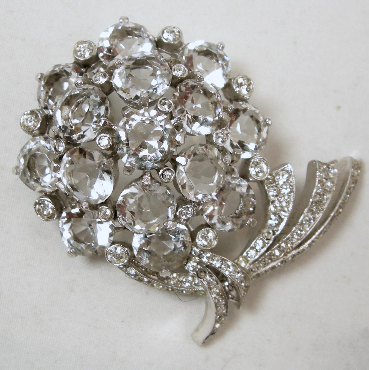 This vintage signed Reja brooch features a floral design with clear crystals in a rhodium silver tone setting.  In excellent condition, this brooch measures 2” x 1-1/2” and is signed “Reja”.