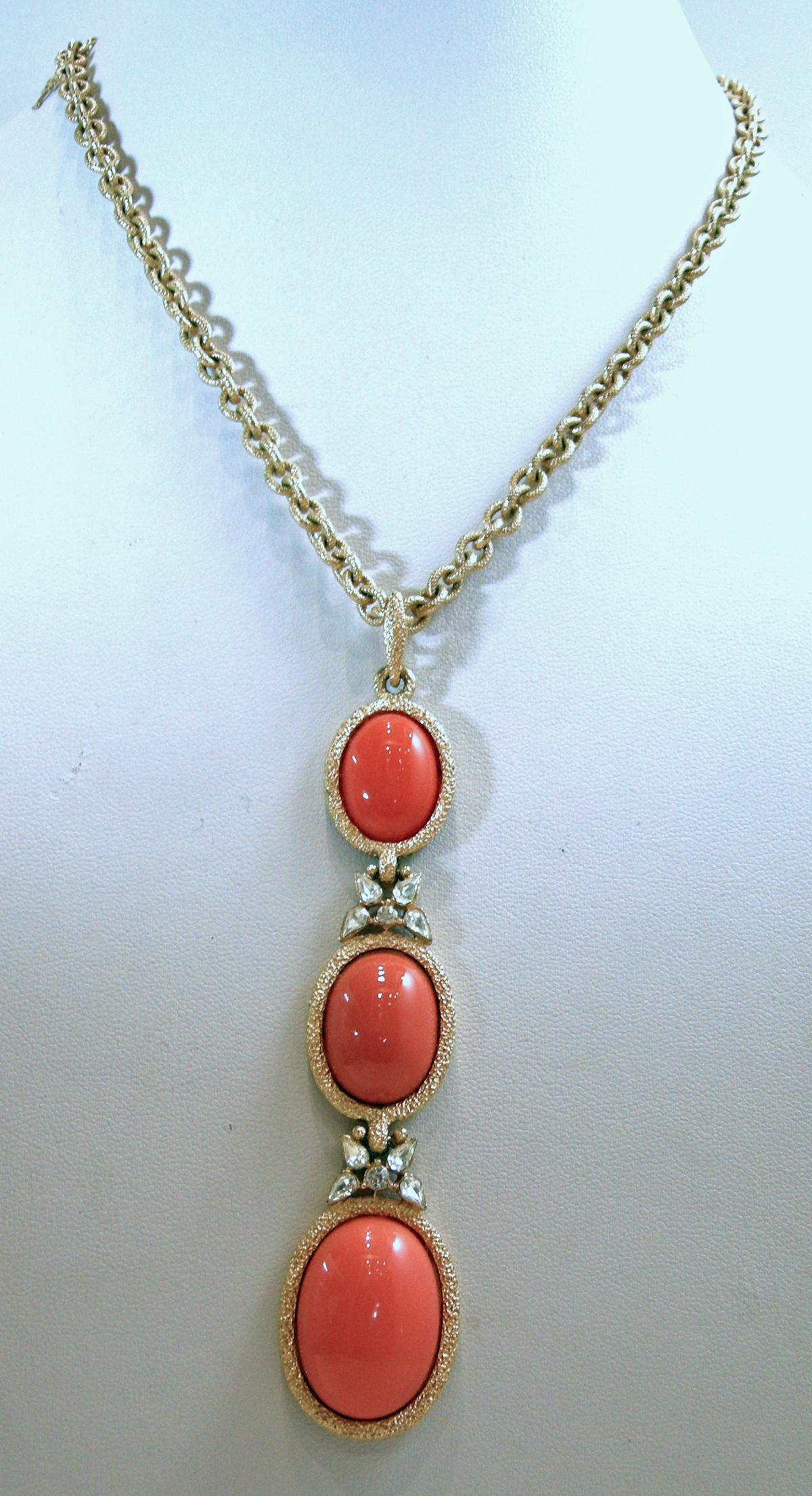 This vintage signed Trifari set has faux coral stones in a gold tone setting.  The necklace has a chain with a centerpiece with three faux coral drops and crystal accents. The necklace measures 16” long with a hook clasp.  The centerpiece is 3-3/4”