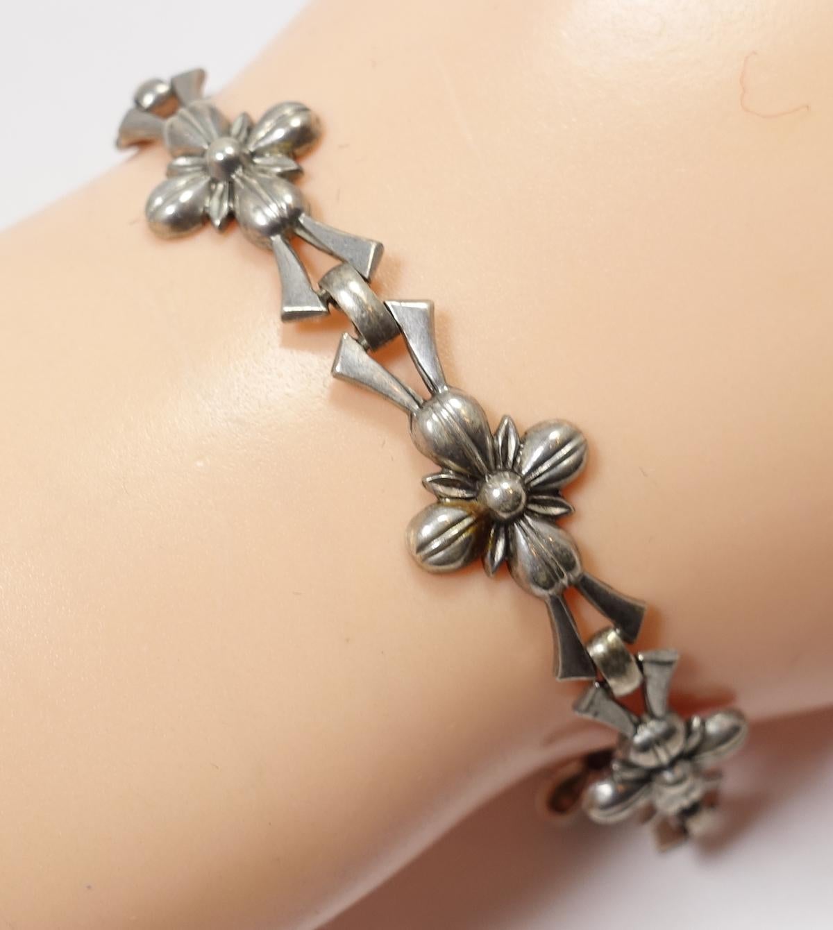 This vintage signed WRE bracelet features multiple floral links in a sterling silver setting.  In excellent condition, this bracelet measures 8” x 1/2” with a fold-over clasp and signed “Sterling WRE”.  
