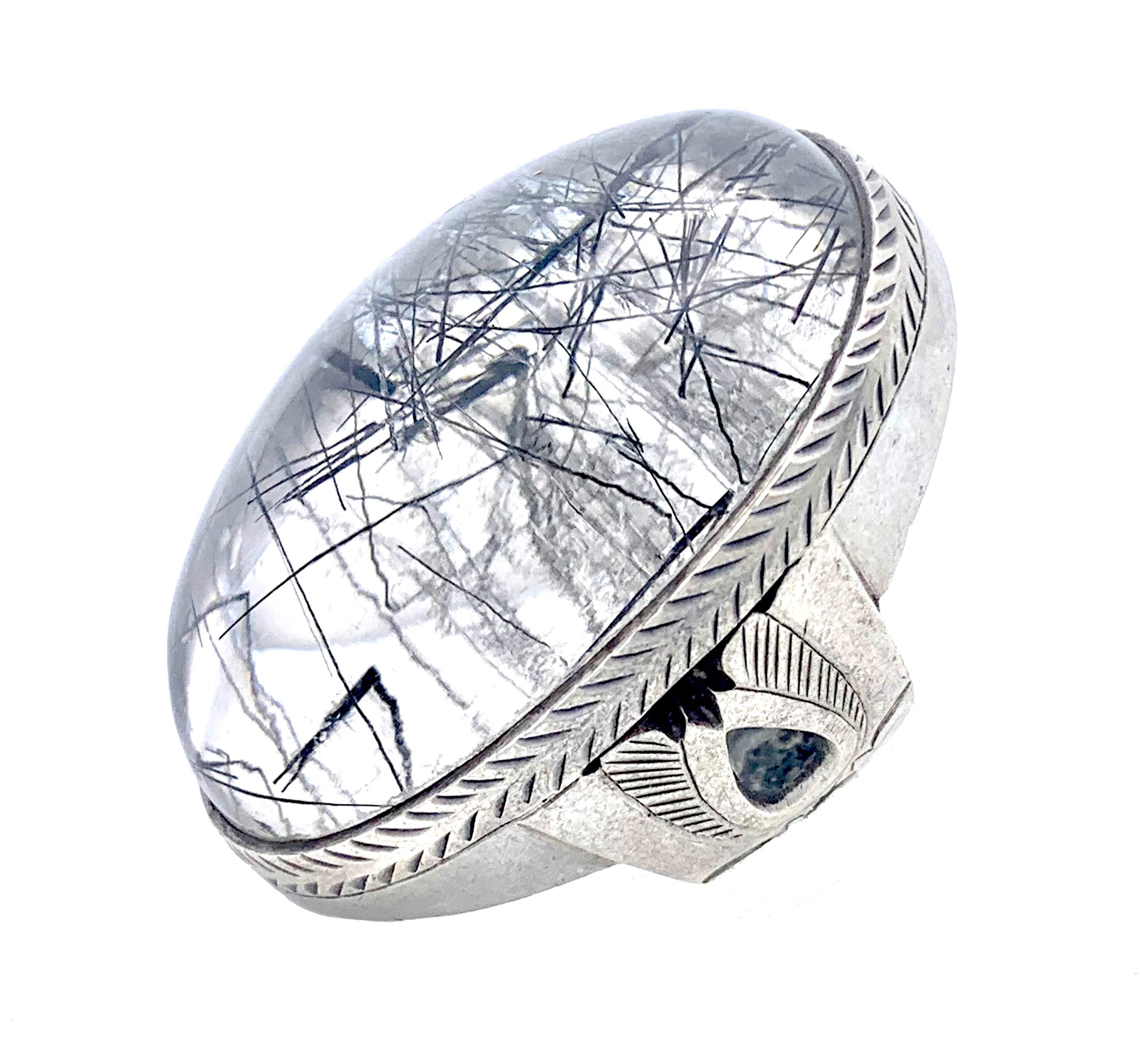 This ring is set with a rutile quarz cabochon in a silver setting engraved with a fishbone pattern. The silver shank is decorated with pierced ornaments and engravings reminiscent of wings. 