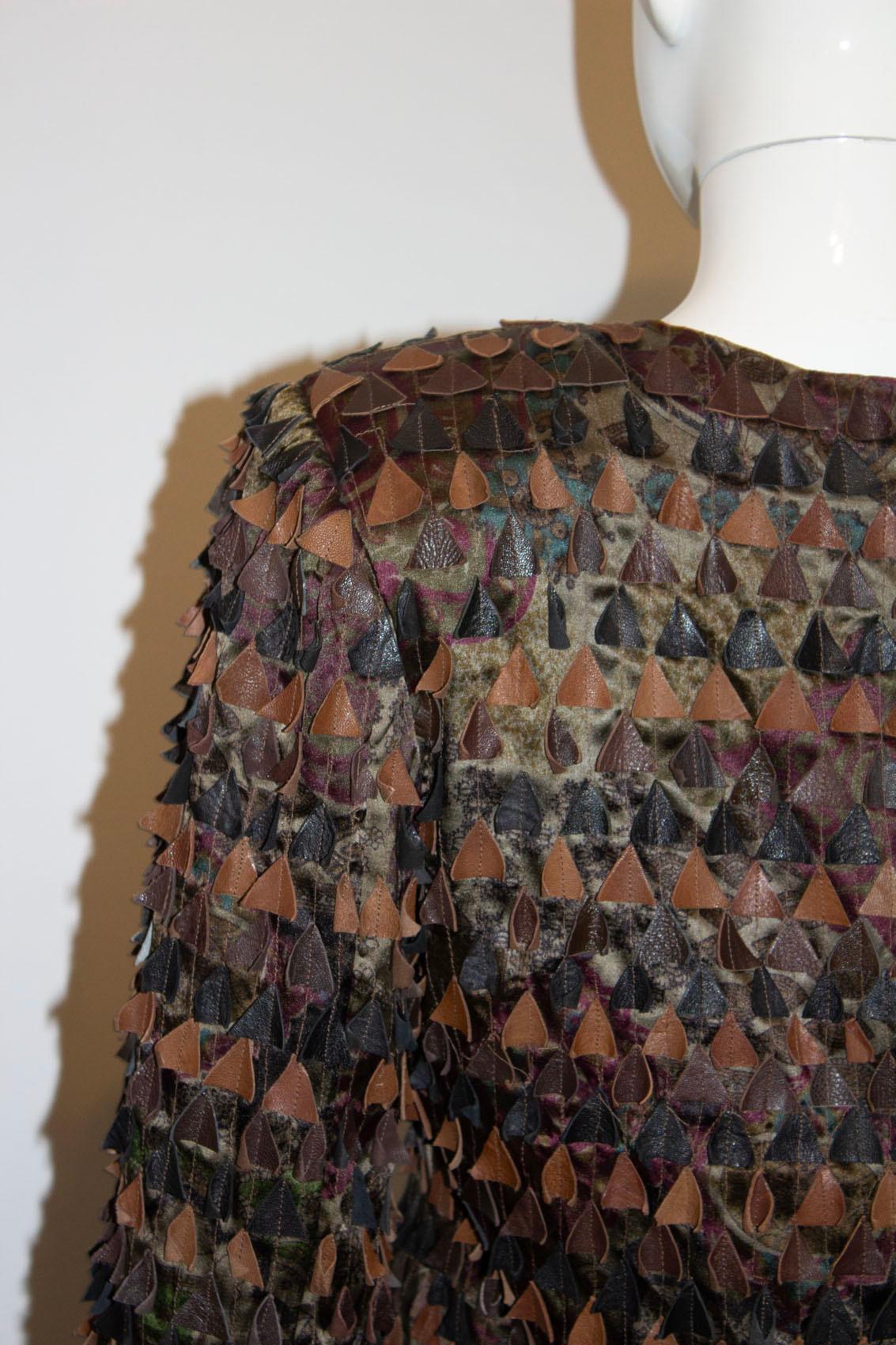 Una estupenda chaqueta vintage de Blank London.
La chaqueta es de seda con un atractivo estampado, y lleva adheridos triángulos de cuero en  varios tonos de oliva y marrón. No tiene cuello, se cierra con automáticos delante y es totalmente  forrado.