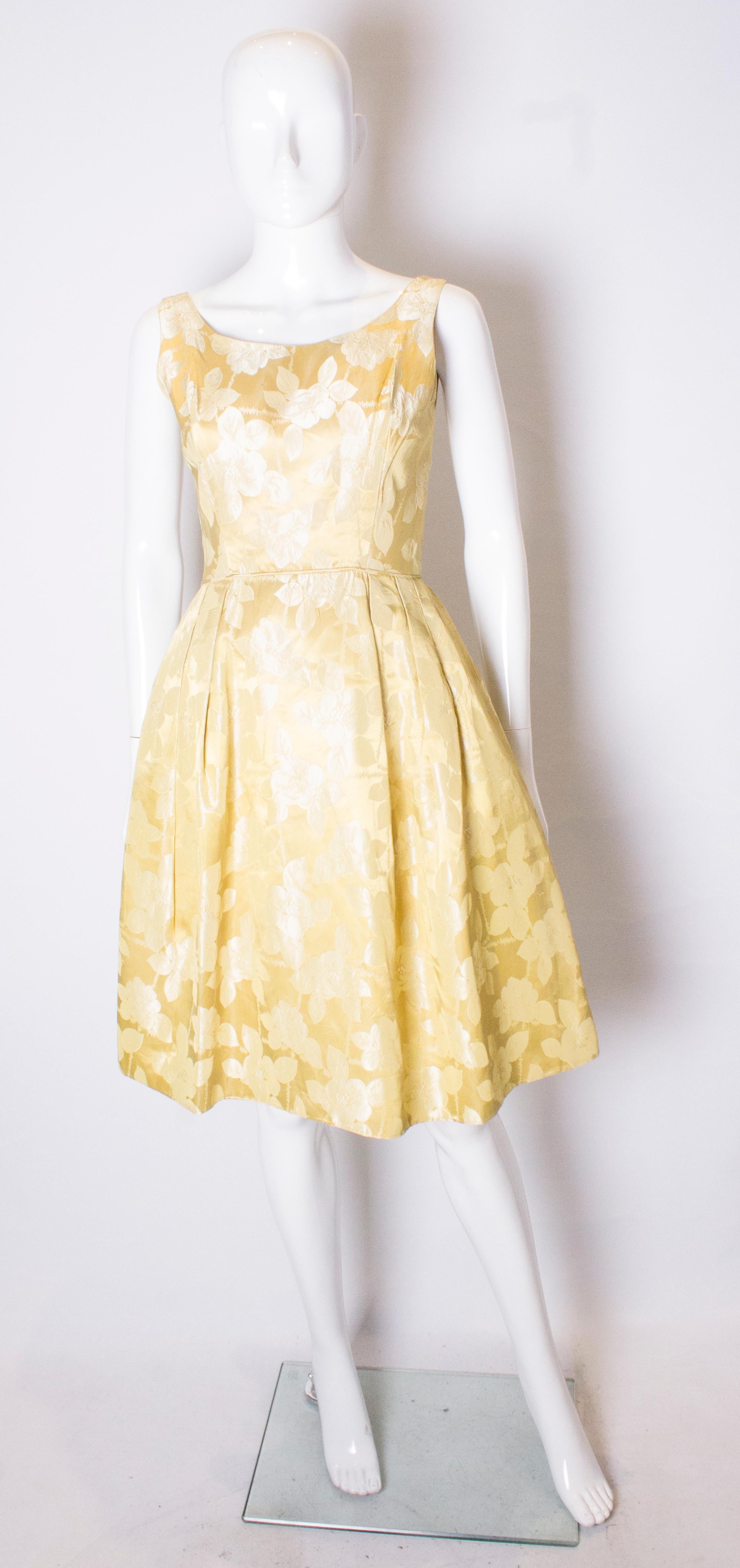 Ein schickes Vintage-Cocktailkleid in einer hübschen gelb/goldenen Farbe. Das Kleid hat einen Rundhalsausschnitt, vorne und hinten mit kleinen Raffungen an der Taille. Es ist vollständig gefüttert, hat einen zentralen Reißverschluss am Rücken und