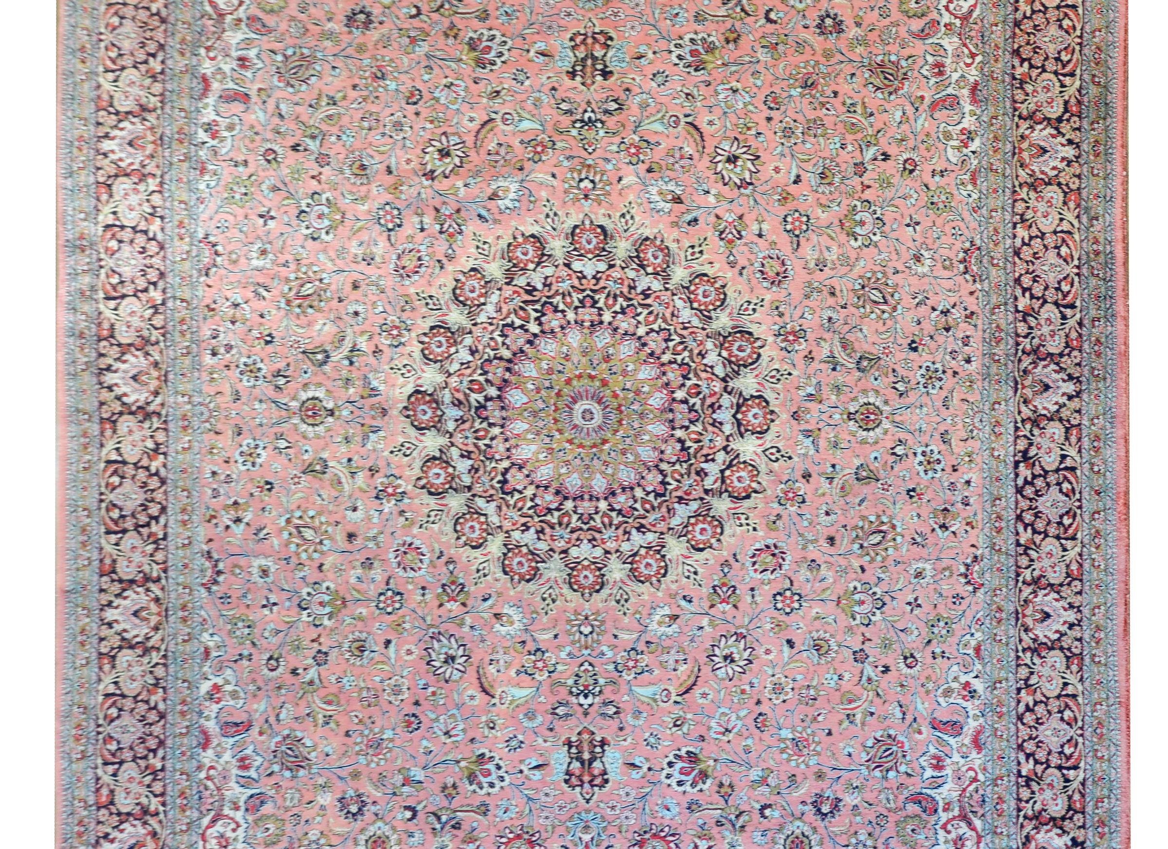 An extraordinary late 20th century hand-knotted silk Qum rug with a mesmerizing central 'rose window' style medallion with amidst a field of intricately woven flowers and vines all woven in indigo gold, crimson, and green, set against a pale pink