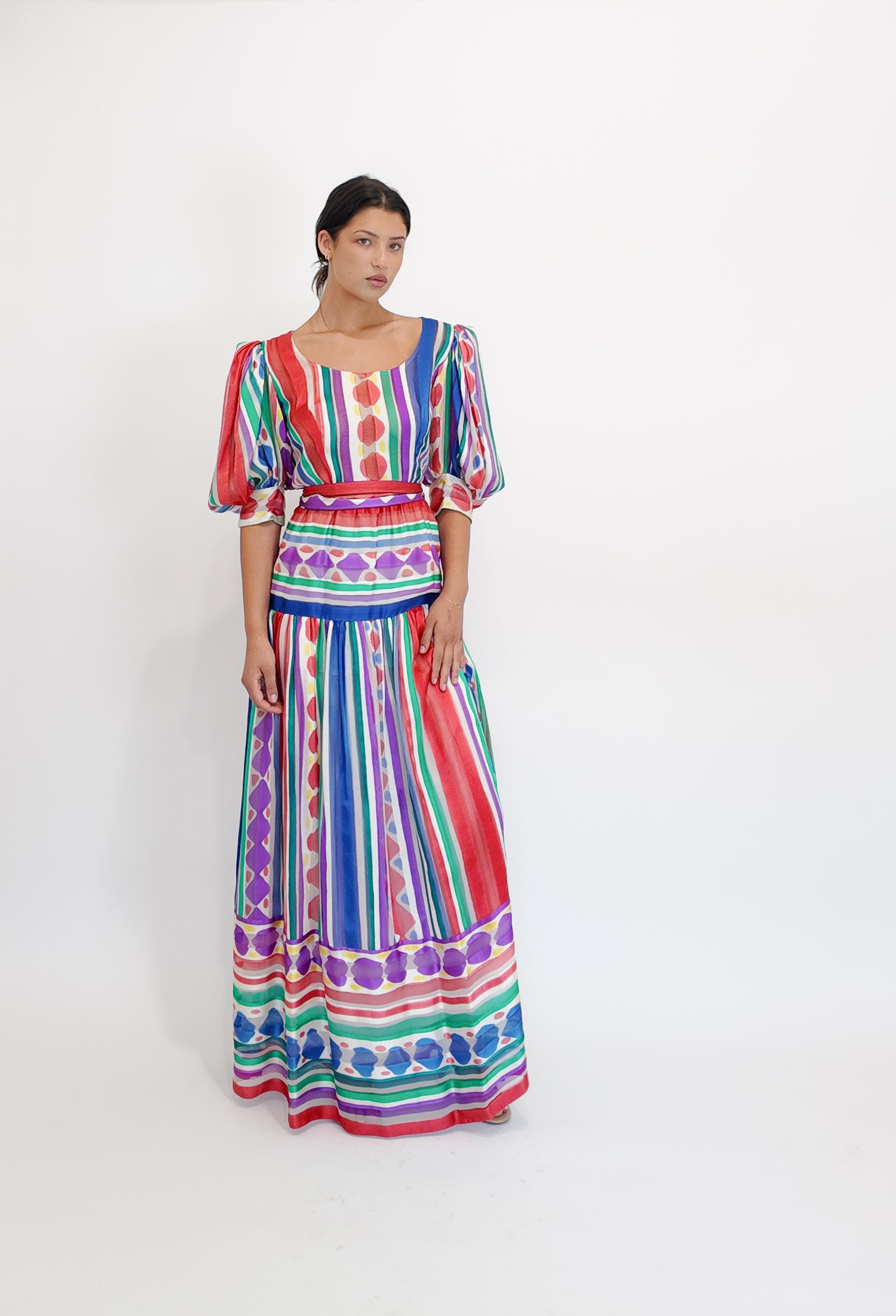 Dieses leuchtende Maxikleid aus Seide besticht durch einen einzigartigen Streifen- und Tupfenprint, der durch Puffärmel und einen passenden Gürtel für eine schmeichelhafte Silhouette ergänzt wird. Sein vielseitiges Design lässt sich mühelos mit