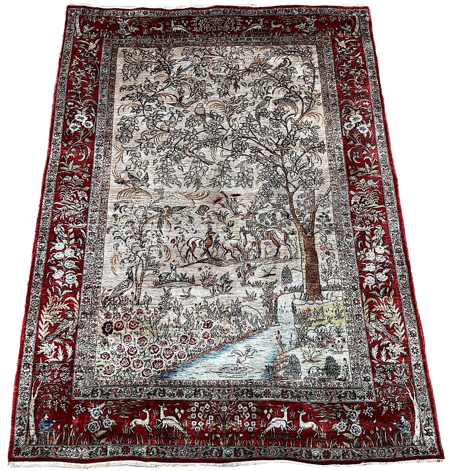 An exceptional silk Qum rug, hand woven in the mid 20th Century. The rug features a classic hunting scene design with all manner of flower and fauna on an ivory field and red border. Finely woven with excellent quality silk, this rug has virtually
