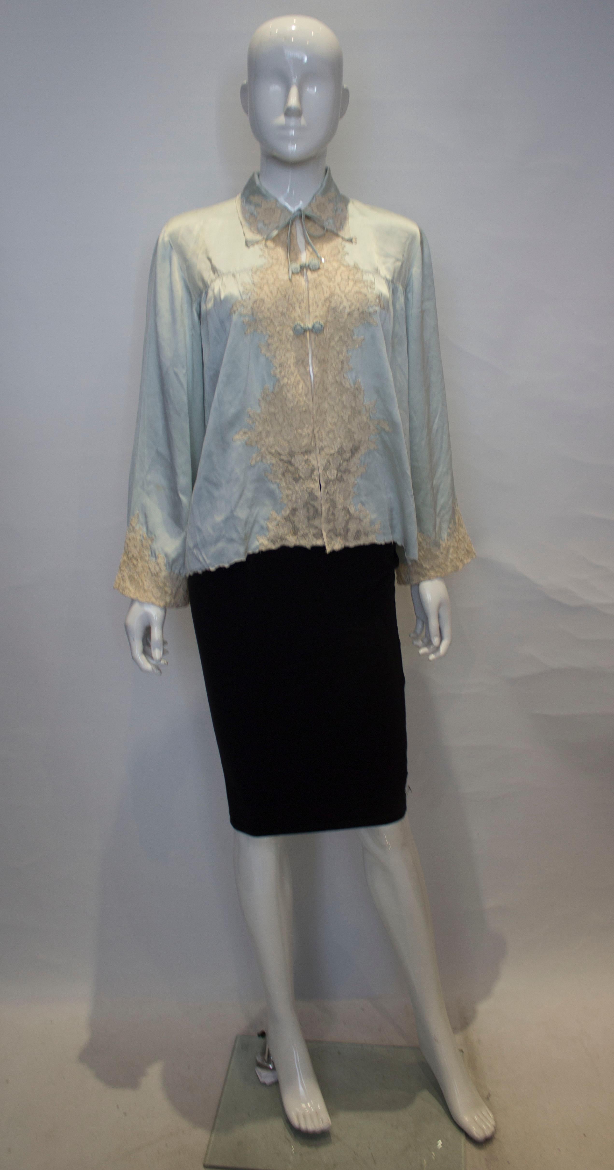 A luxurious vintage silk satin bed jacket with lace detail in a pretty ice blue colour. The jacket has a tie opening at the top and two toggle on the front. There is wonderful lace detail on the front and cuffs, with pleats from the yoke and a