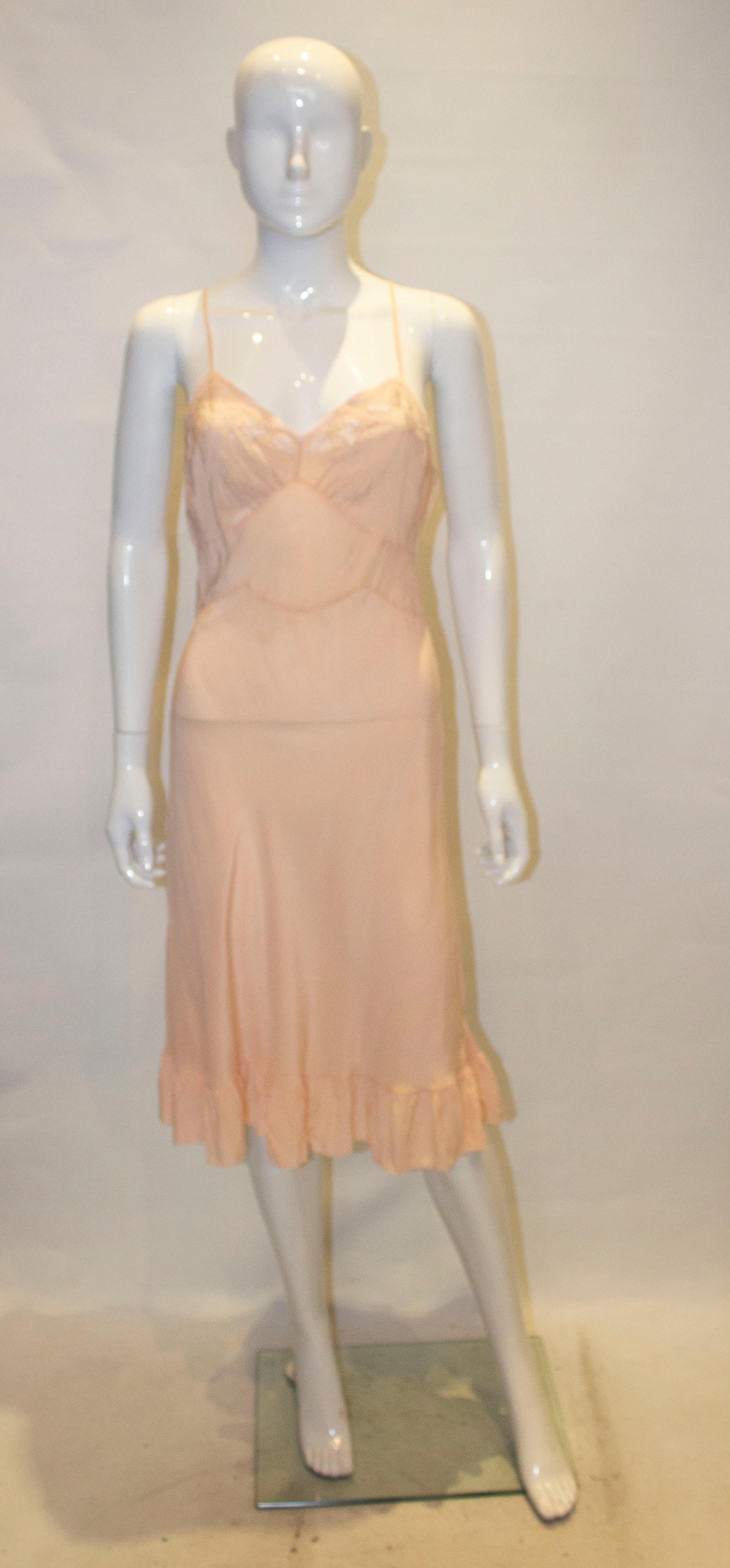 Ein Vintage-Slipkleid aus Seide in einer hübschen Pfirsichfarbe.  Das Slip-Kleid hat einen V-Ausschnitt mit Stickerei im Brustbereich und eine Rüsche am Saum.