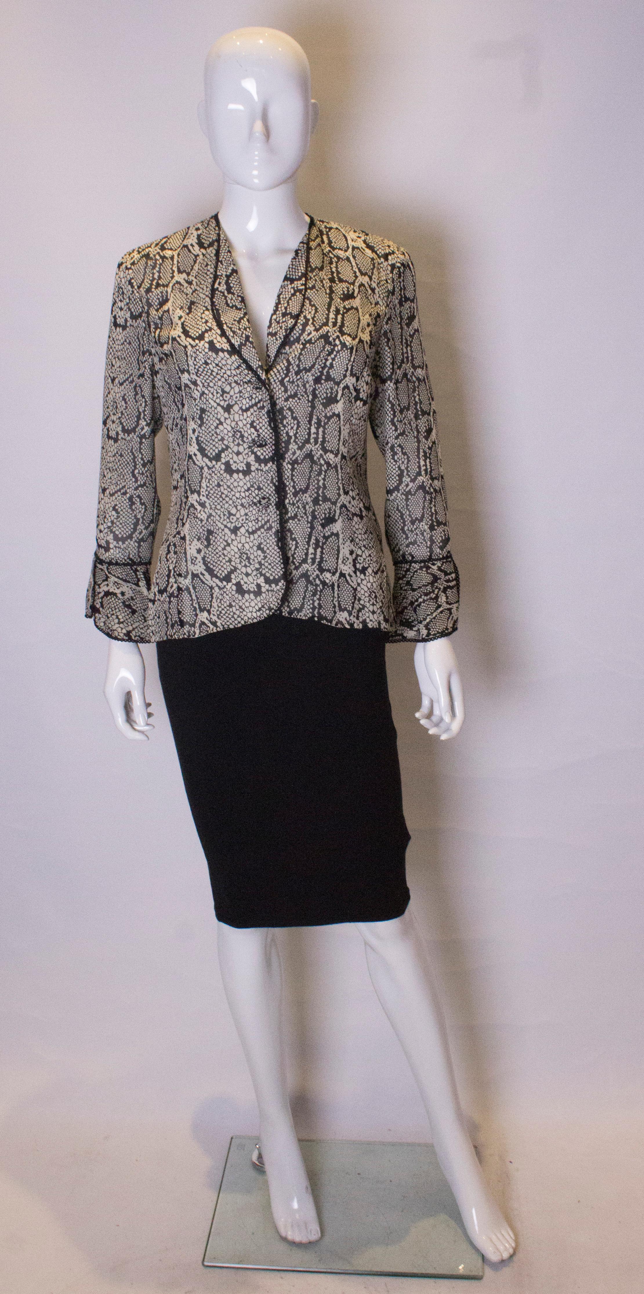 A chic jacket in silk by Caroline Charles. The jacket is in an attractive snakeskin print with cut away low collar, and frilled turnback cuffs. It is fully lined and edged in black.